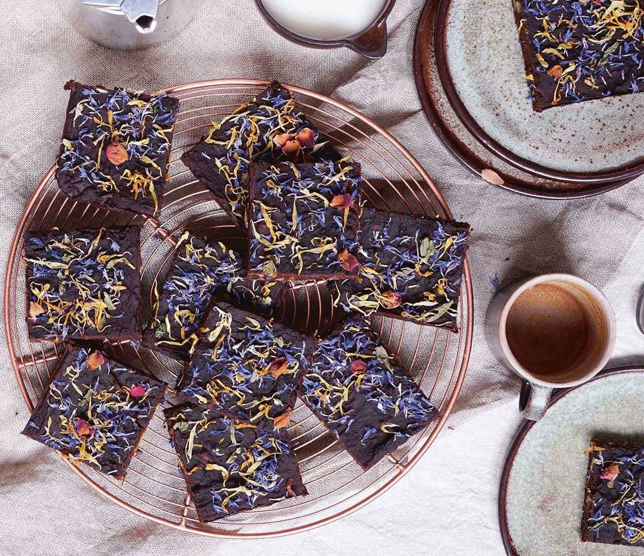 Squares of dark brownie topped with edible flowers on a copper plate