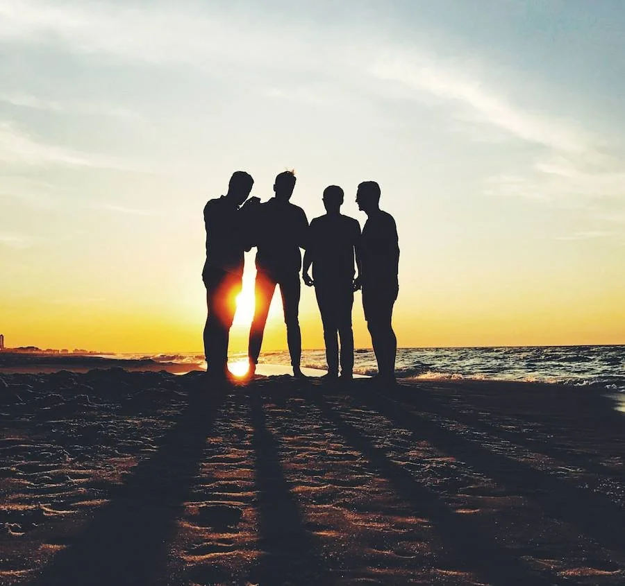 Silhouettes of four men standing together on a beach at sunset