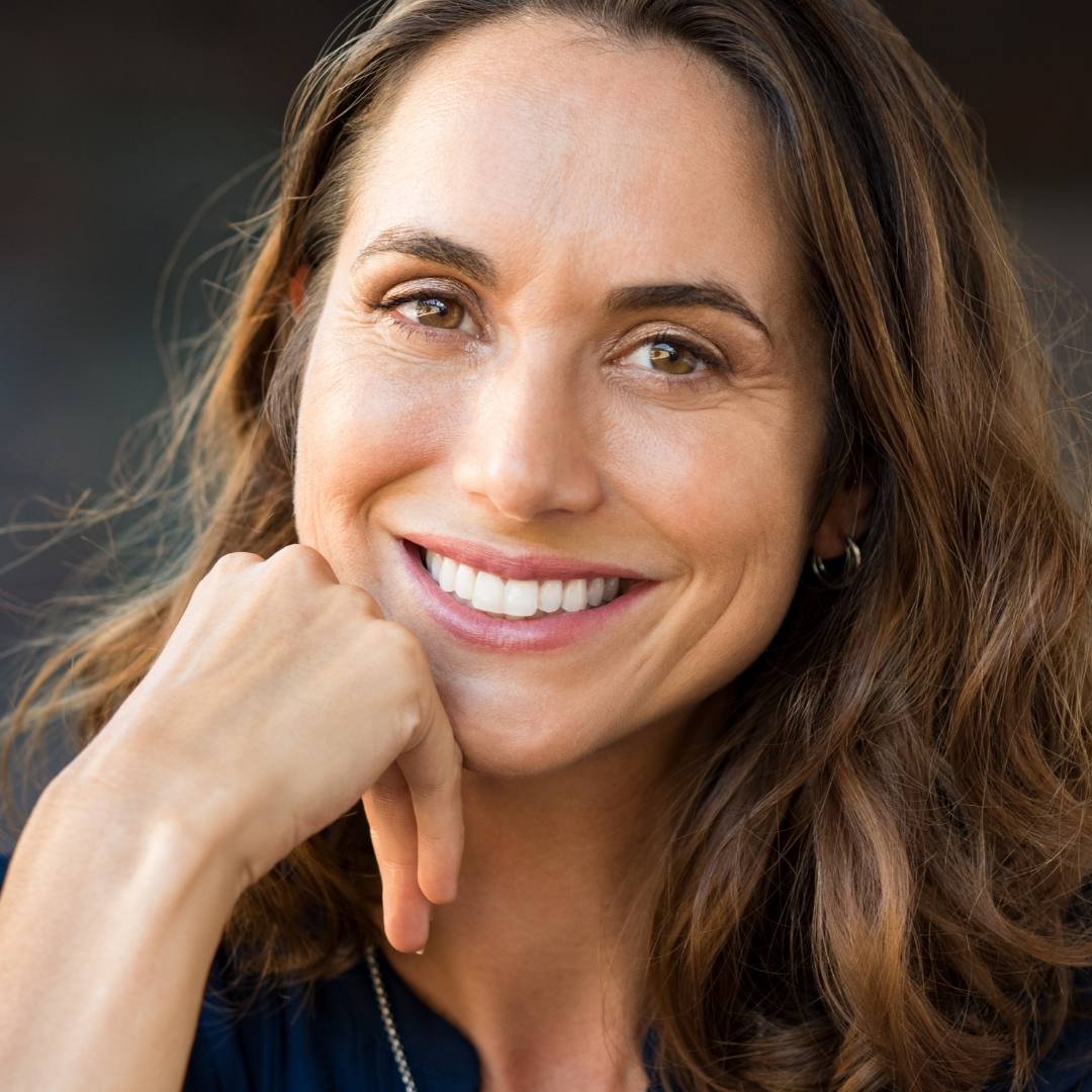 Smiling woman with long brown hair resting her chin on one hand
