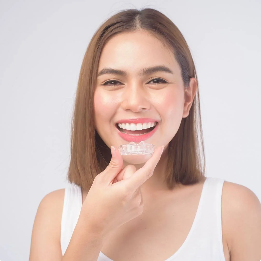 Smiling woman holding a clear aligner tray beside her straight teeth
