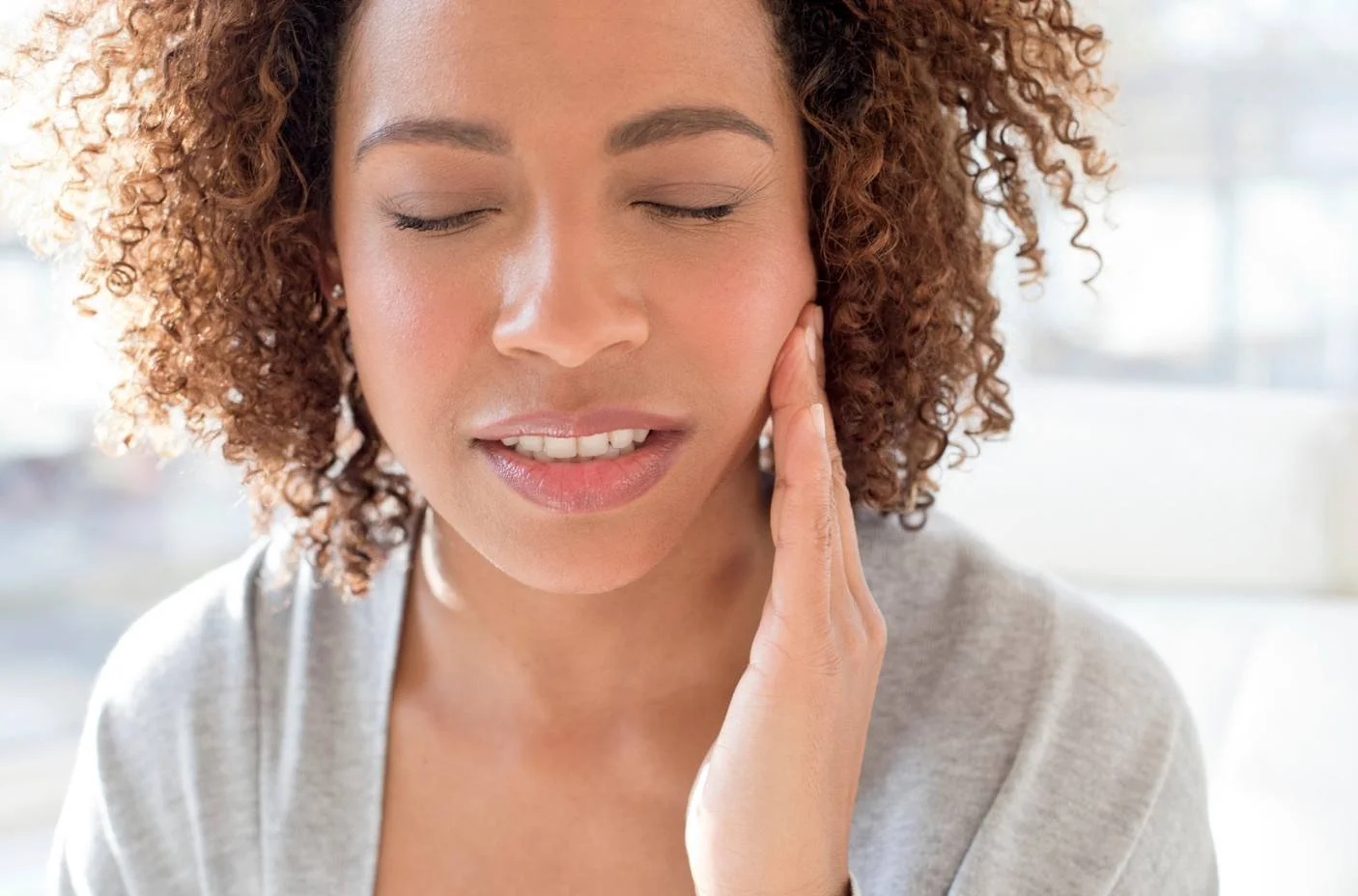 Woman with curly hair pressing a hand to her aching cheek