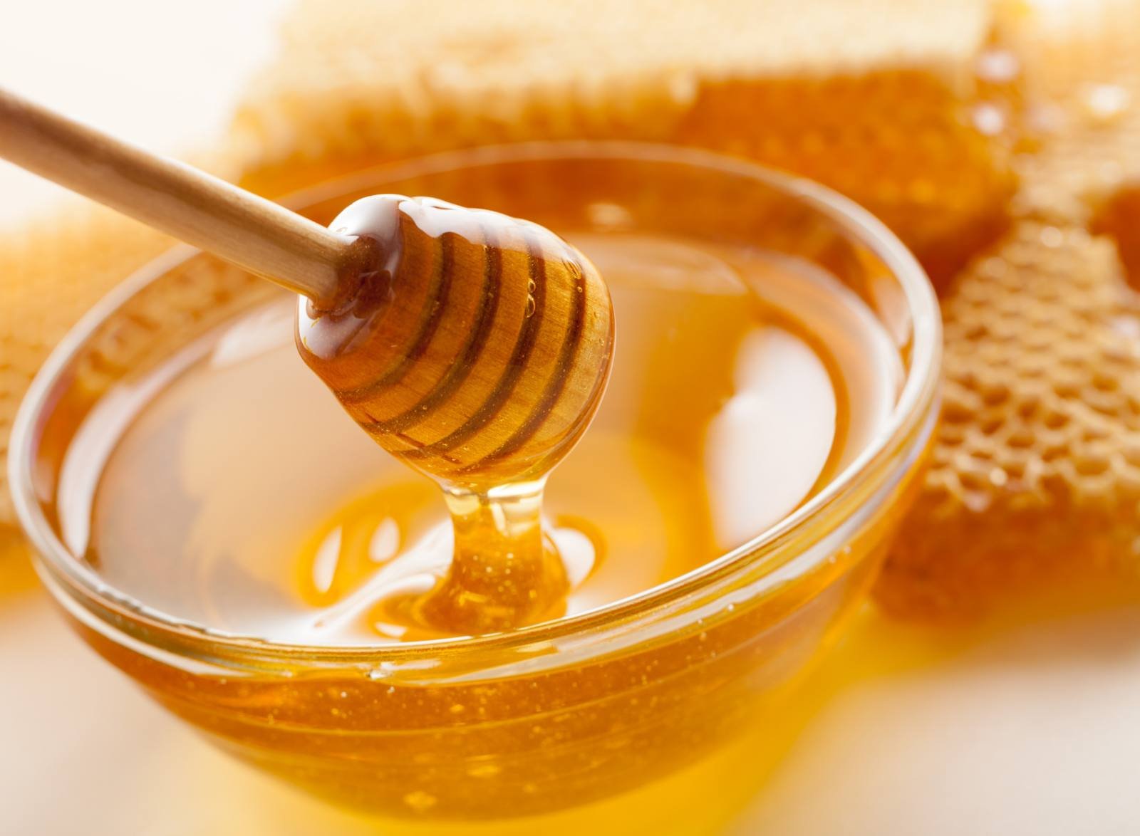 Wooden dipper resting in a bowl of honey beside fresh honeycomb