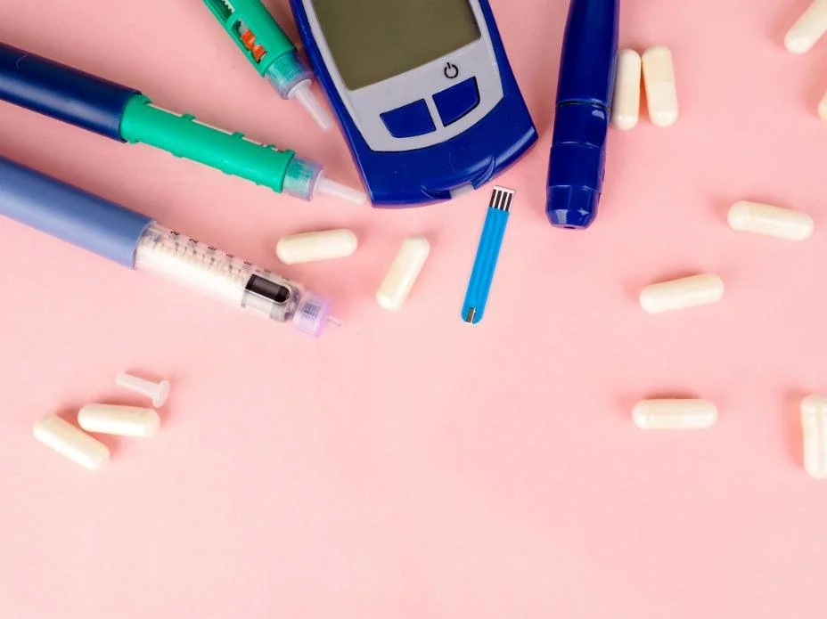 Glucose meter, insulin pens and tablets laid out on a pink surface
