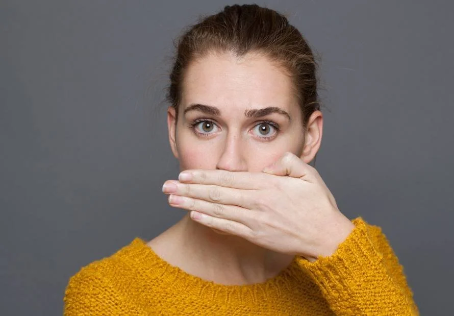 Woman in a yellow jumper covering her mouth with one hand