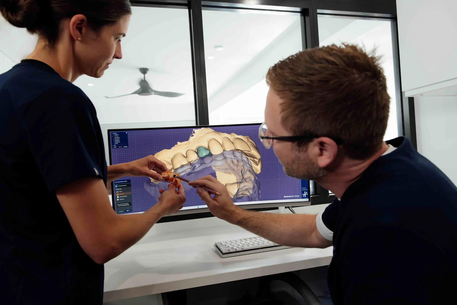 Two of our team comparing a printed model of a patient’s teeth with a crown design on screen
