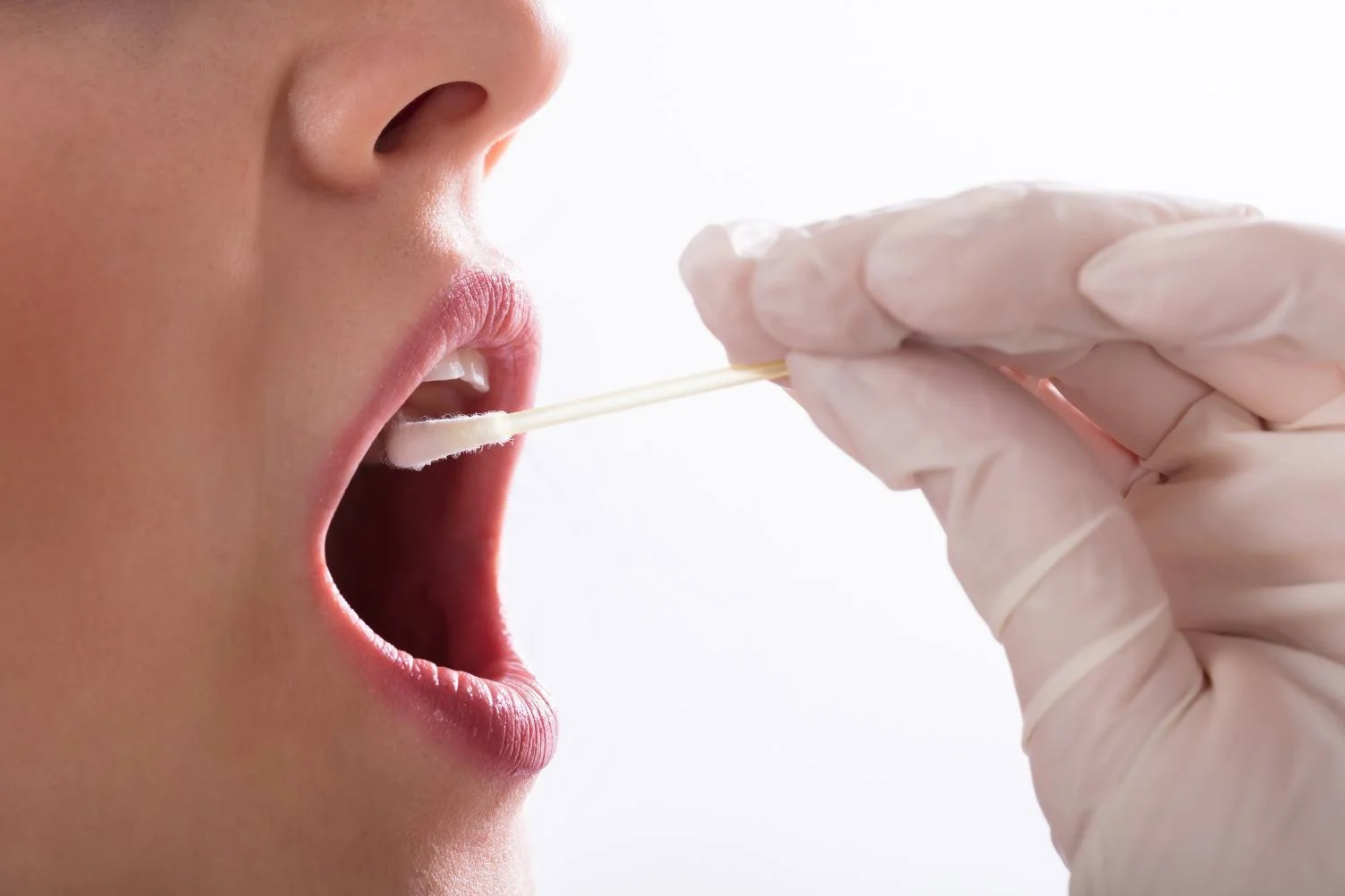 Gloved hand taking a swab sample from a person's open mouth