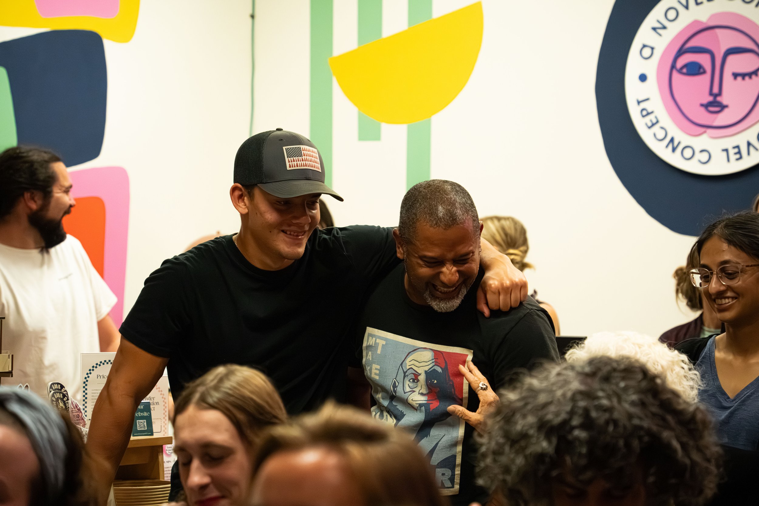 A son congratulating his father after a stellar performance reading his comedic poem that made the whole room laugh at A Novel Concept's poetry slam with the Poetry Room on September 19th, 2025 in Lansing, Mich.