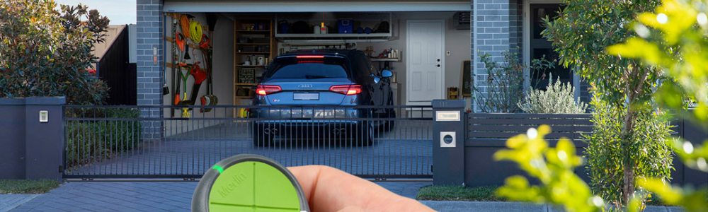 Homeowner using a Merlin garage door remote to open a modern double garage, showing a parked car and secure residential driveway.