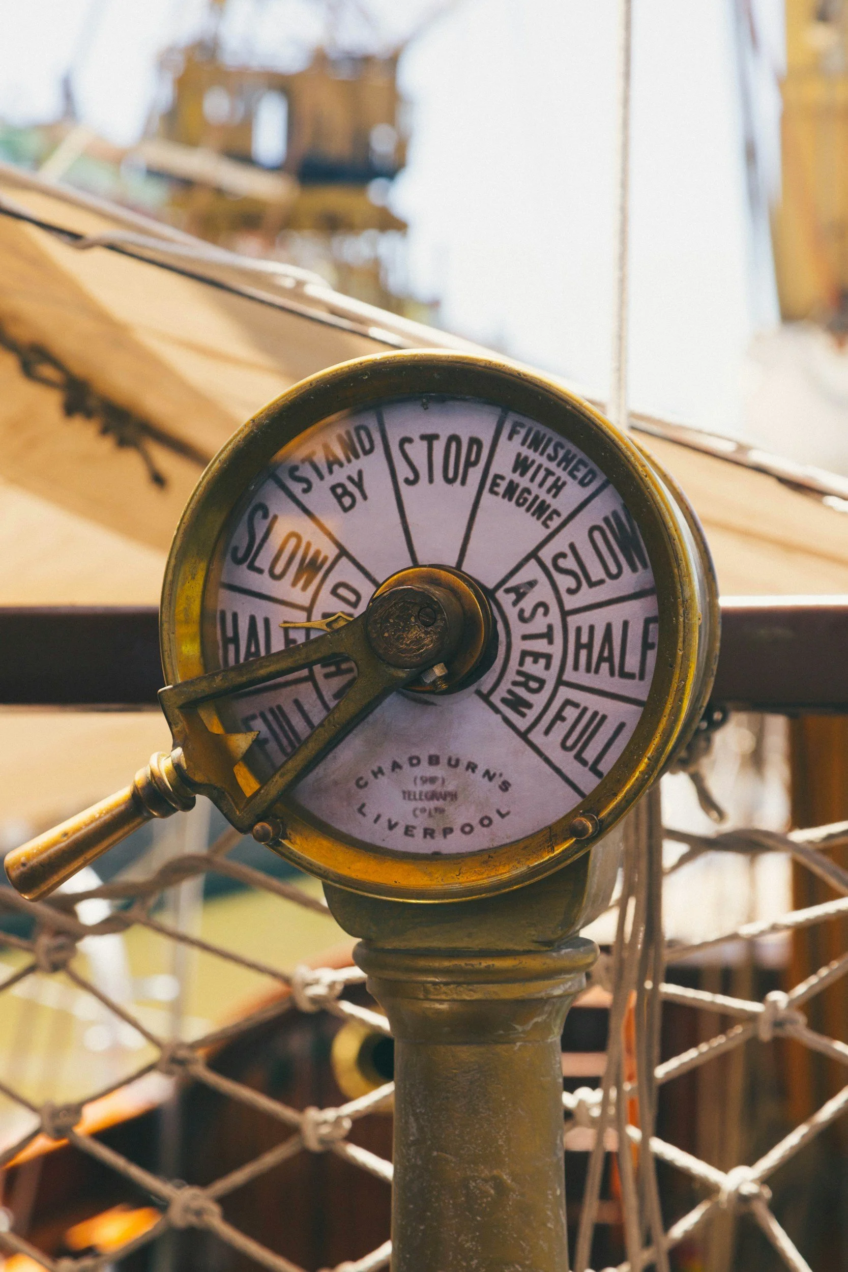 Vintage transportation fare or clock device with segmented labels indicating stops from full to stop, with some sections labeled half, slow, and stand by, mounted on a pole with a background of ropes and blurred outdoor scenery.