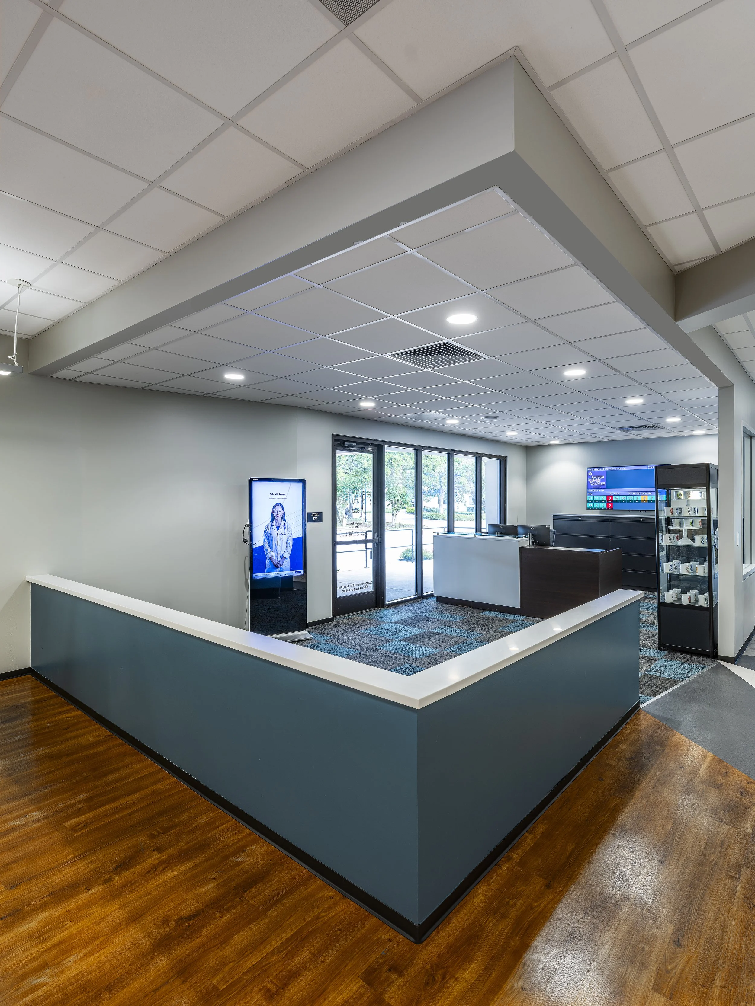 Interior of a modern medical office or clinic with a reception area, digital health display, and entry doors.