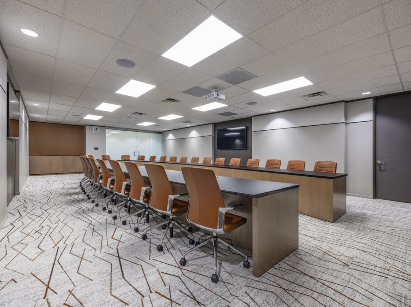 Empty conference room with long tables, orange chairs, a large wall-mounted TV, and ceiling lights.