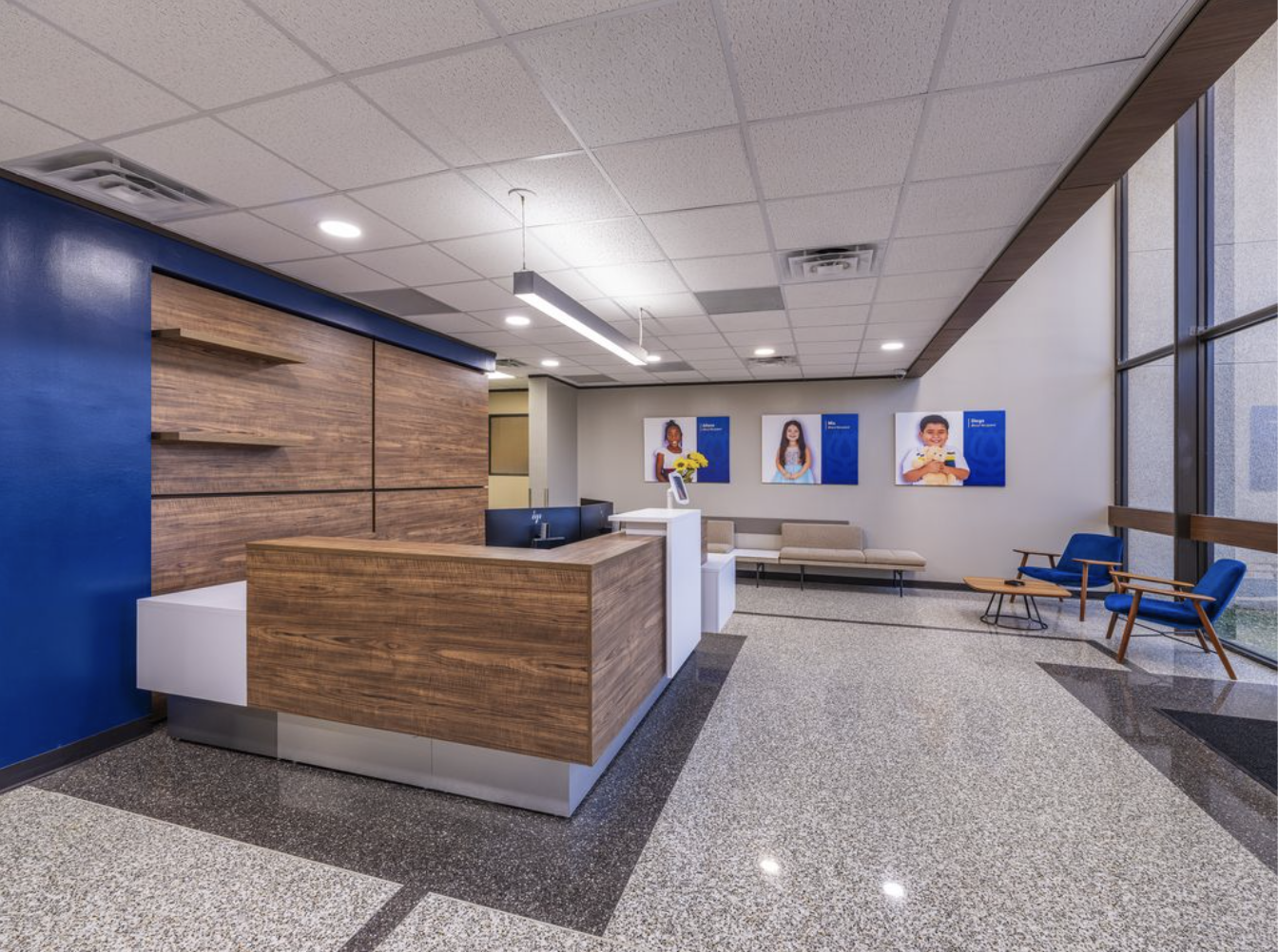 Hospital or clinic reception area with a wooden desk, seating area, and wall art featuring children.