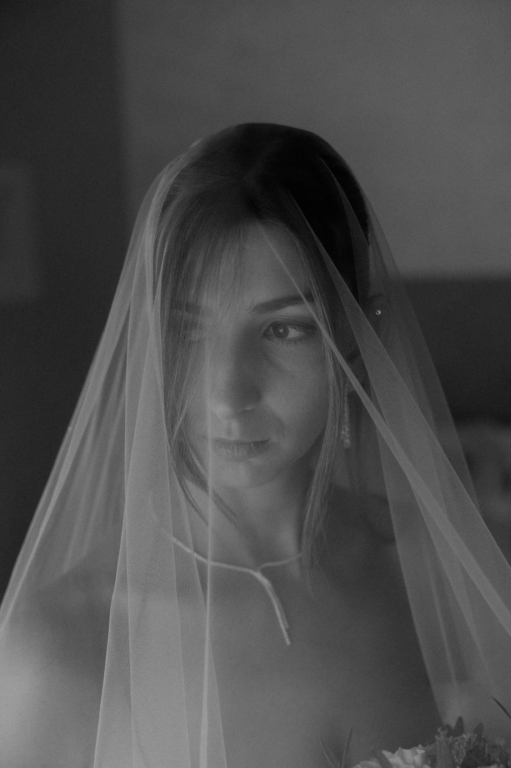 Black and white photo of a woman with short hair, partially covered by a semi-transparent veil, looking to the side with a soft smile.