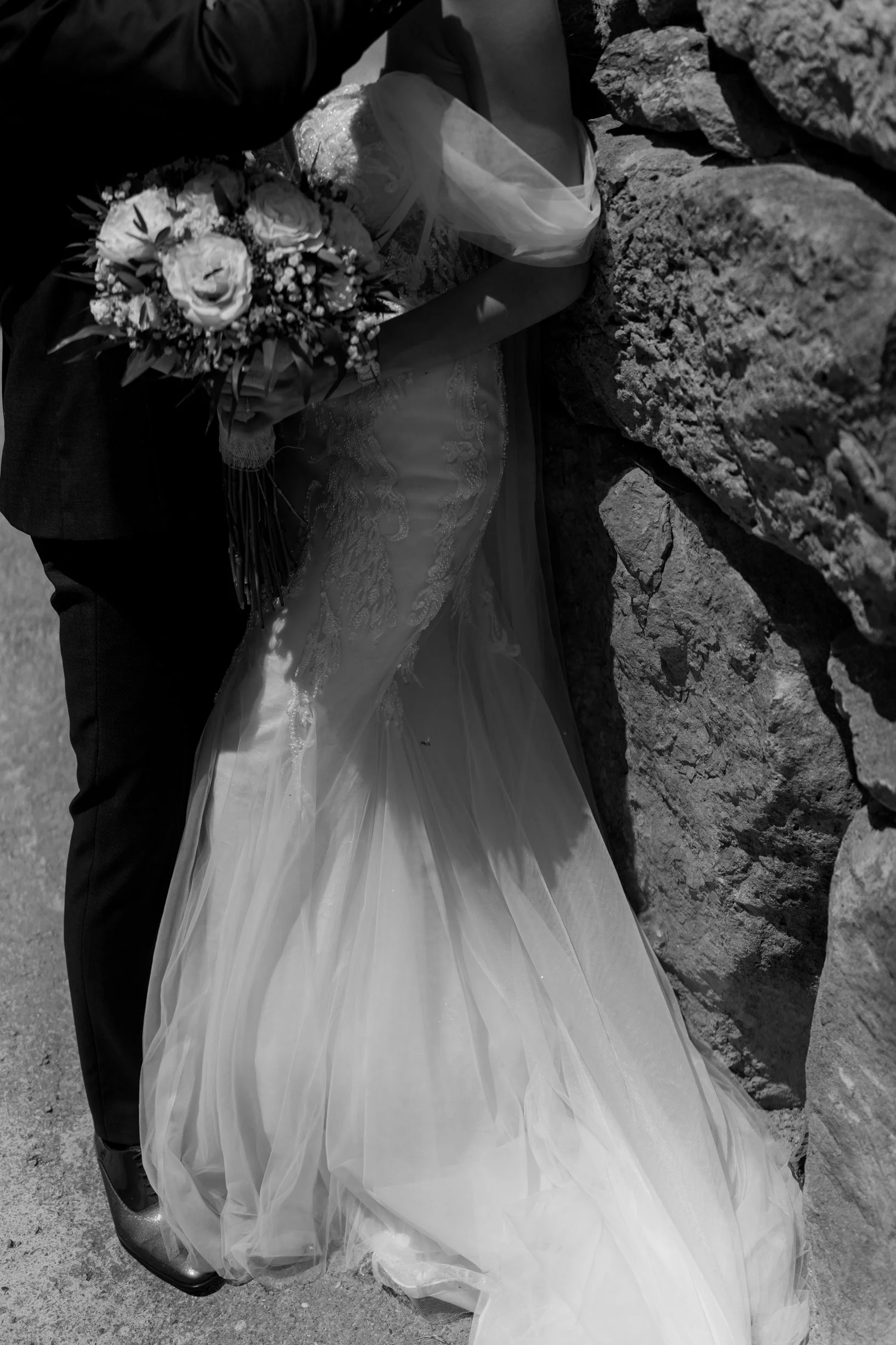 A bride in a wedding dress holding a bouquet of flowers, standing next to a rocky wall.