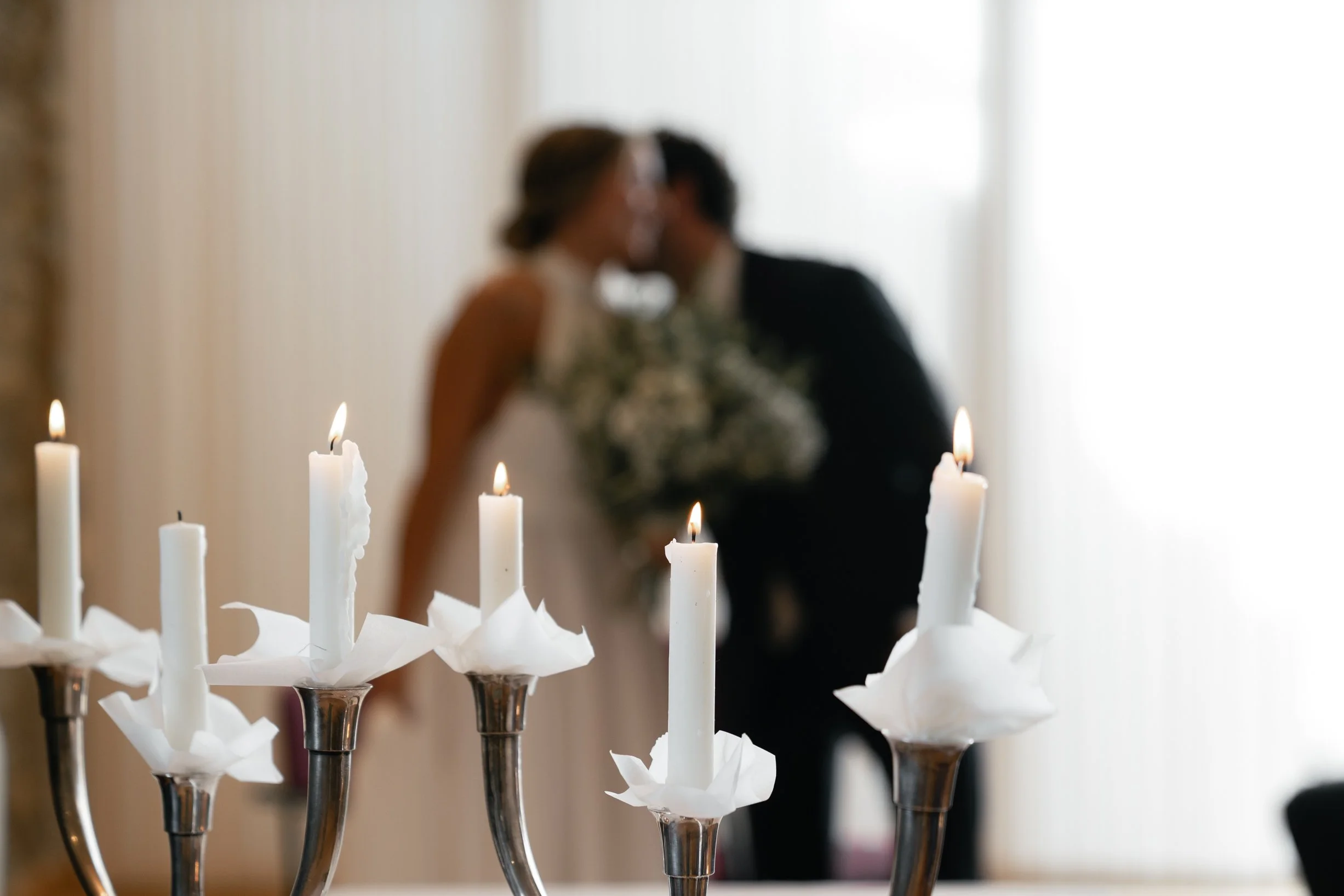 Blurred couple kissing in the background with lit candles in focus in the foreground