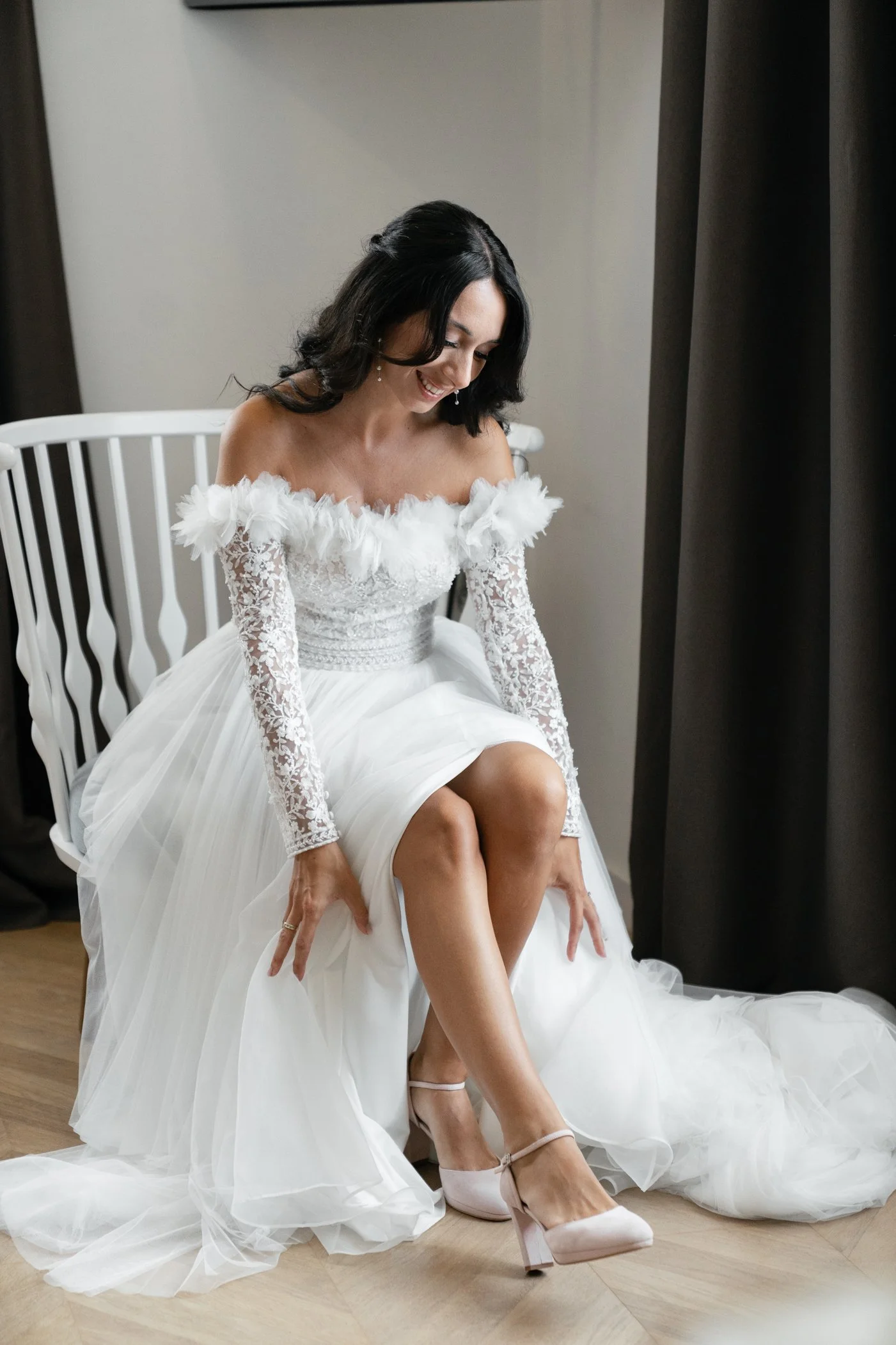 A woman in a wedding dress sitting on a chair, adjusting her shoe.
