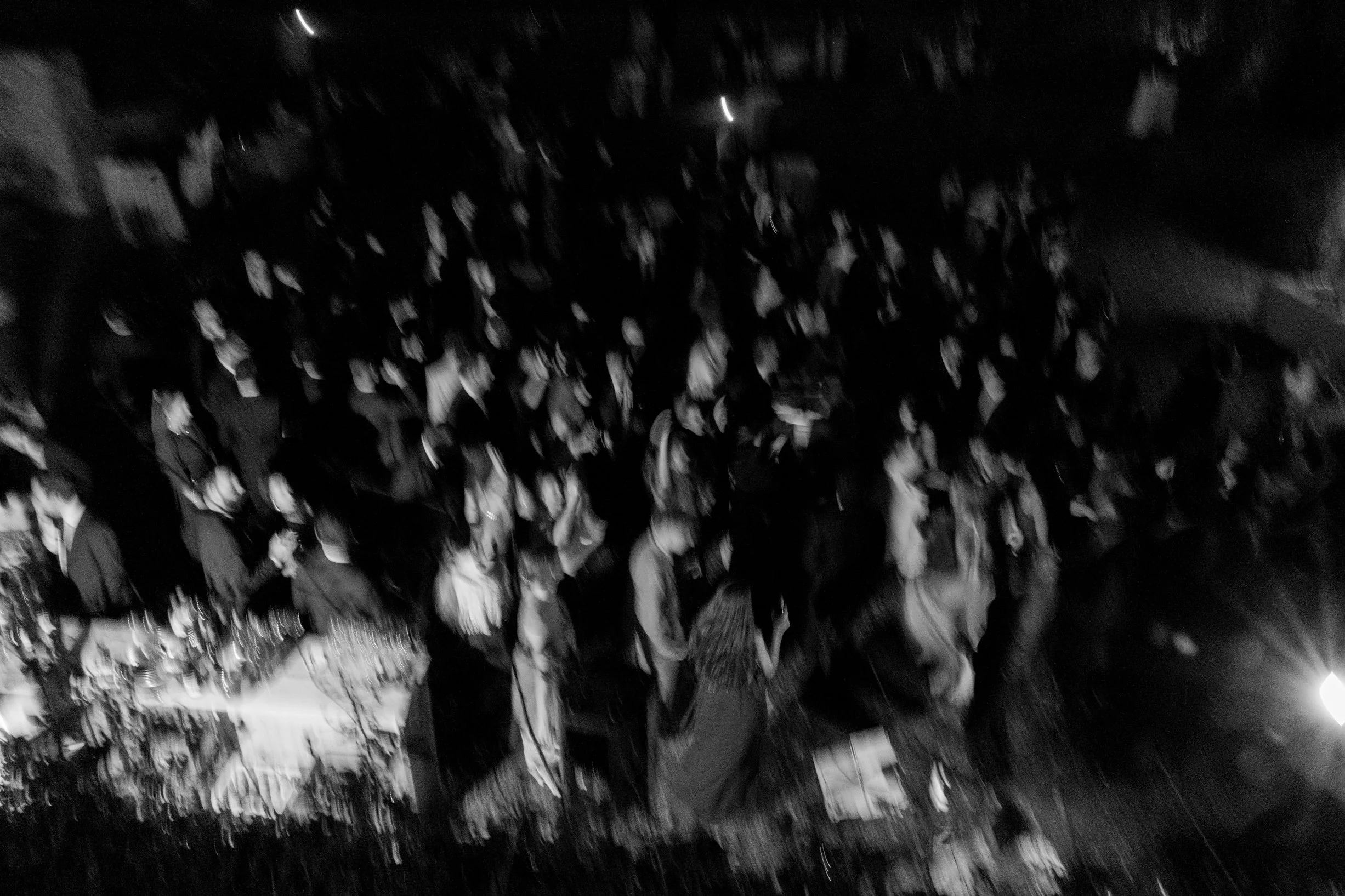 A large crowd of people gathered outdoors at night, with some looking forward and others talking, illuminated by artificial lights.