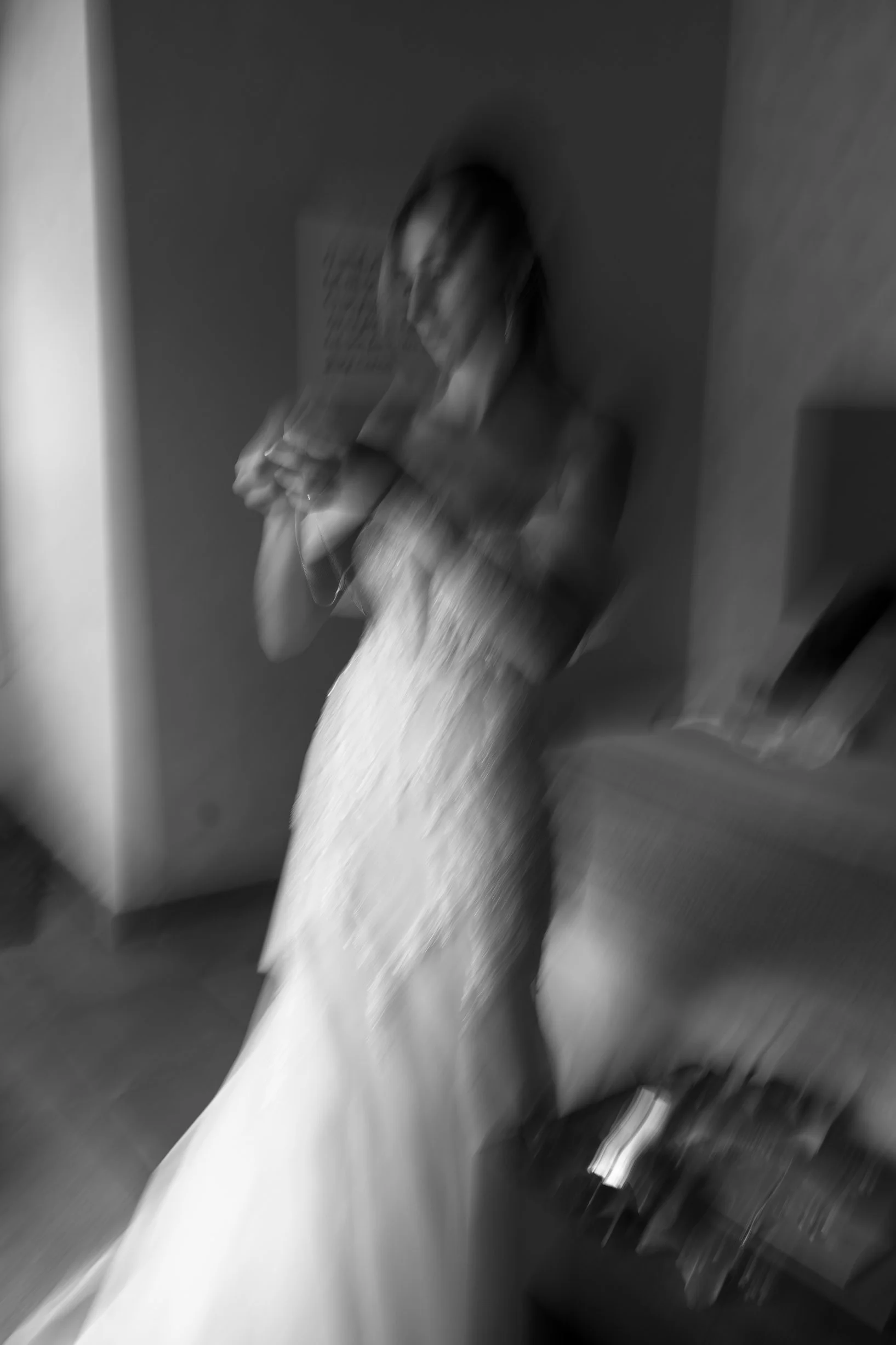 A blurry black-and-white photo of a woman in a dress looking at her phone.
