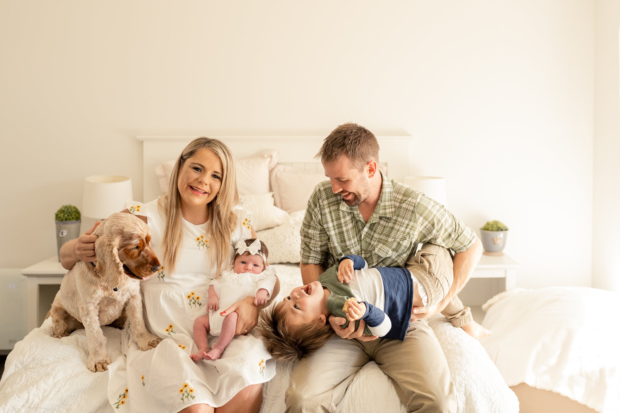 A mother and father with their two kids and dog sitting on a bed.