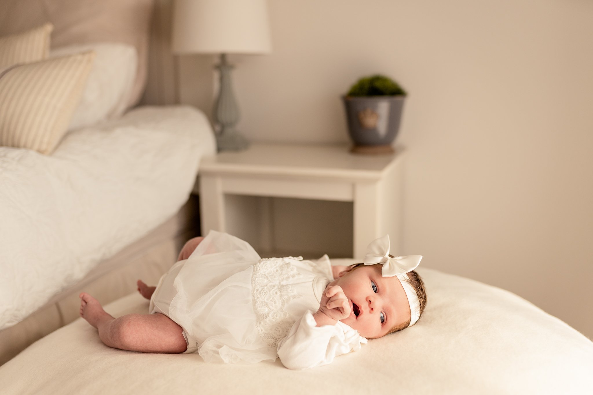 A baby girl in a white dress lying on a beanbag.