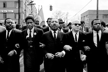 Black and white photo of civil rights leaders linking arms during a march, representing collective action for equality and justice.