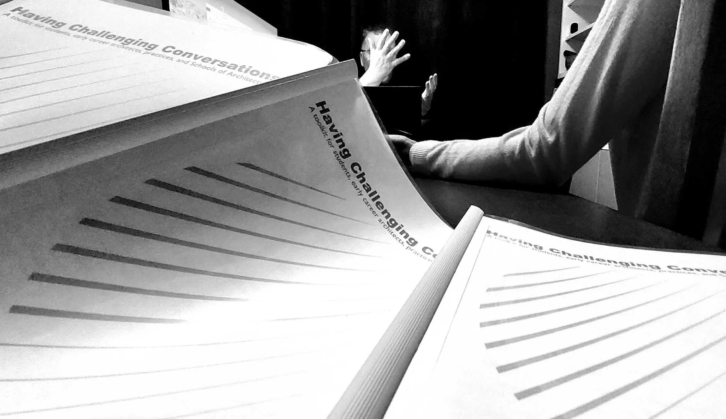 Black and white photo of “Having Challenging Conversations” toolkit handouts on a table during a workshop discussion.