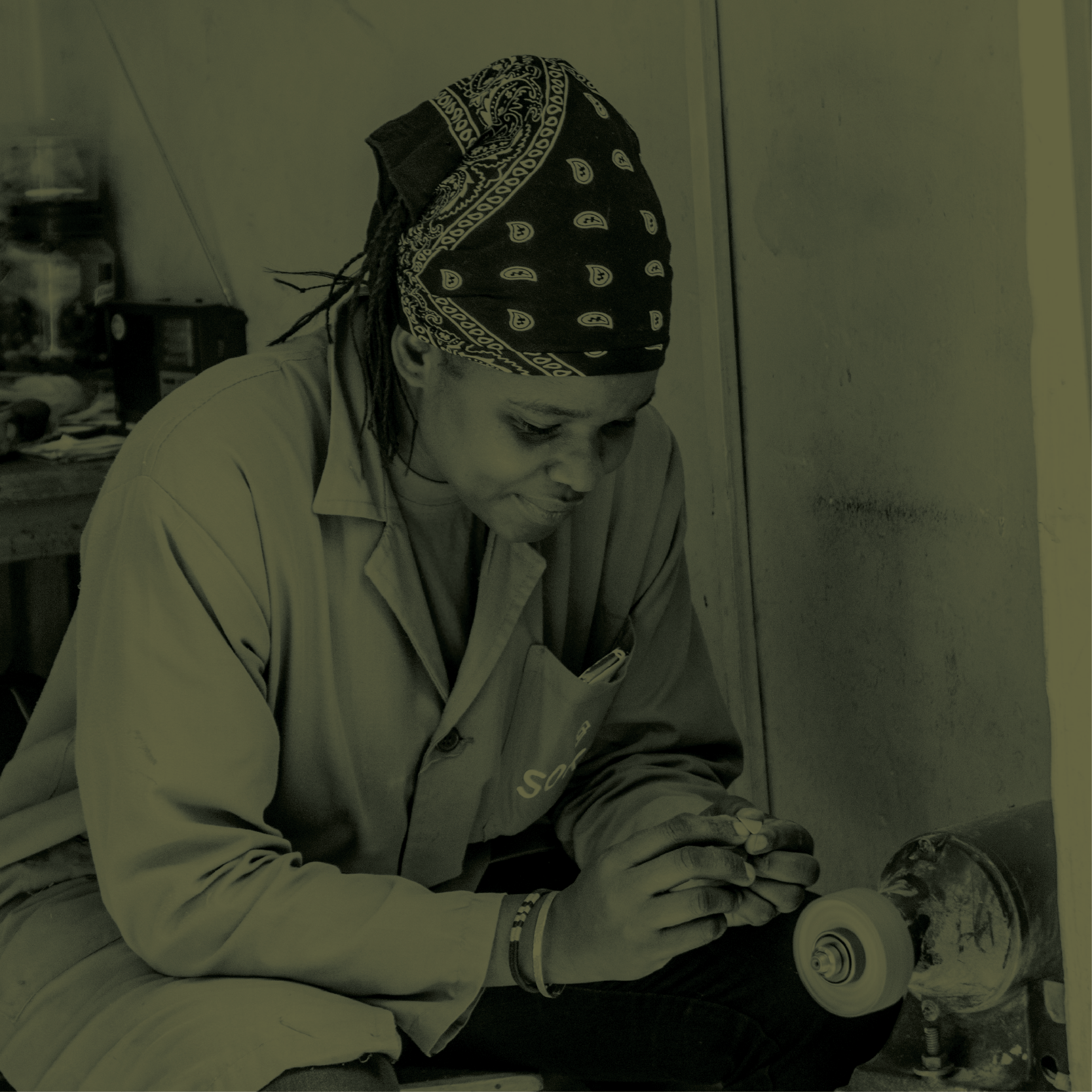 A person wearing a black bandana with white patterns, working with a grinding tool on an object, in an indoor workshop.