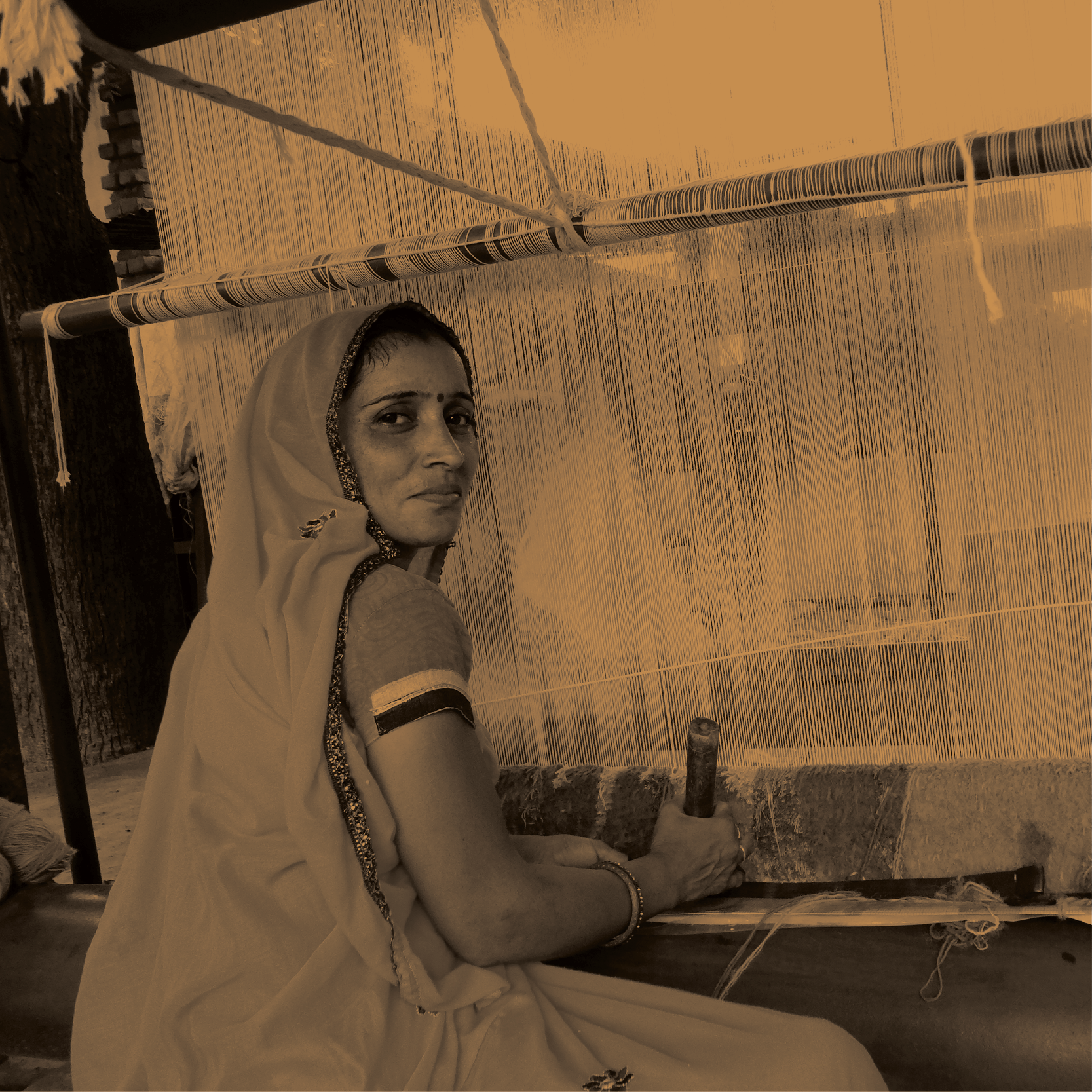 An Indian woman wearing traditional attire working on a weaving loom.