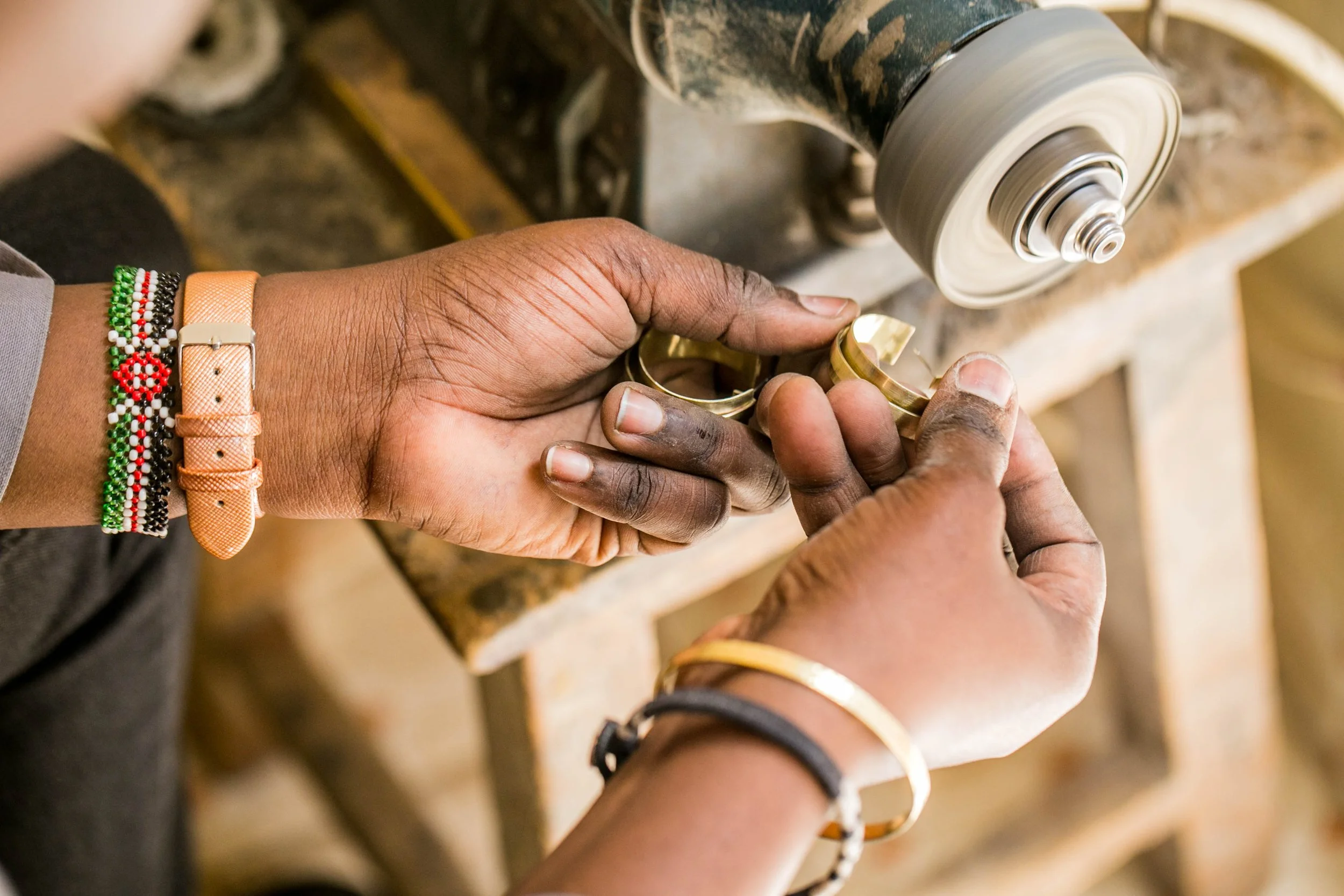 Person shaping a gold bracelet on a rotating jewelry polishing machine in a workshop.