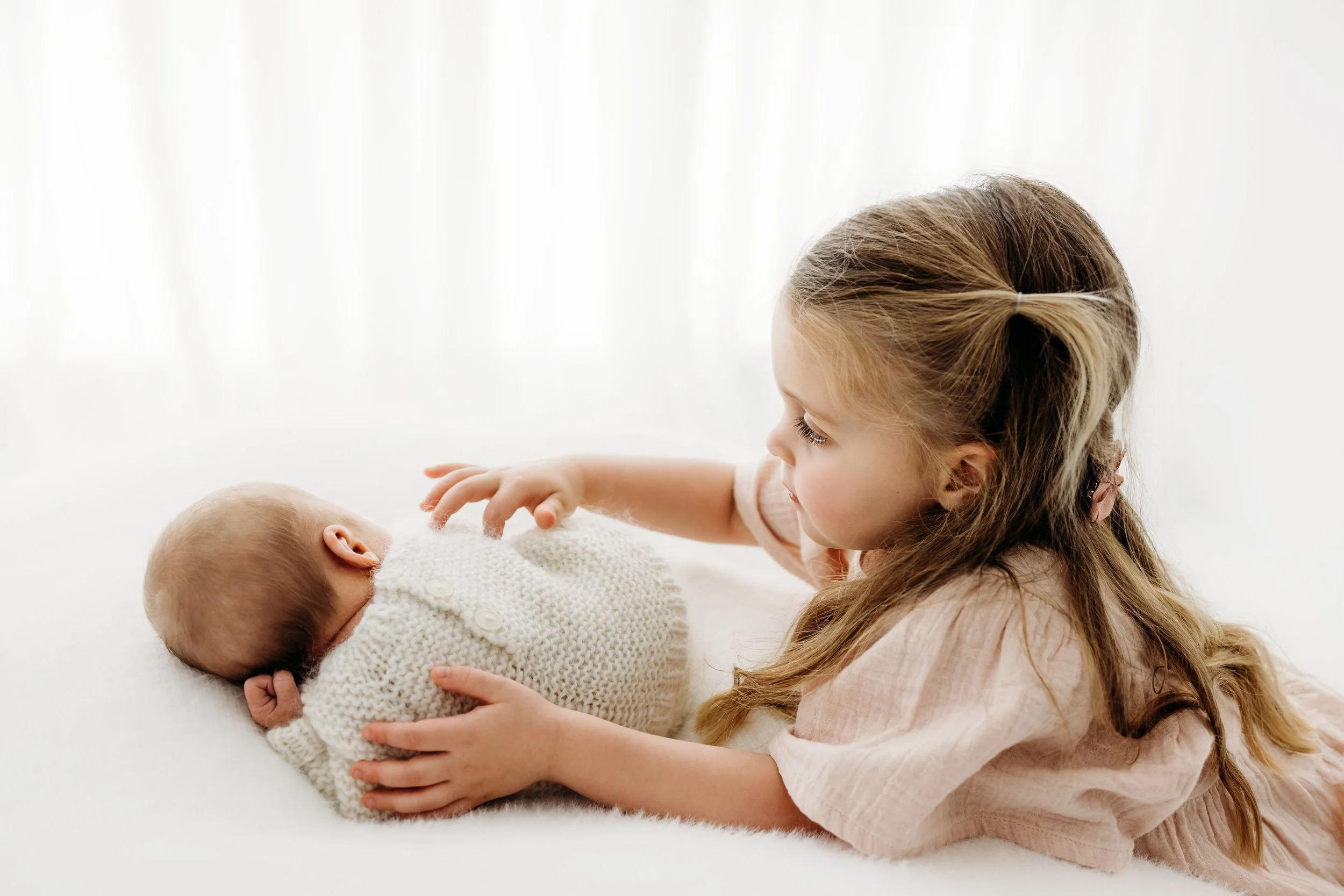 Older sibling cuddling their newborn baby during a newborn family photography session in Perth.