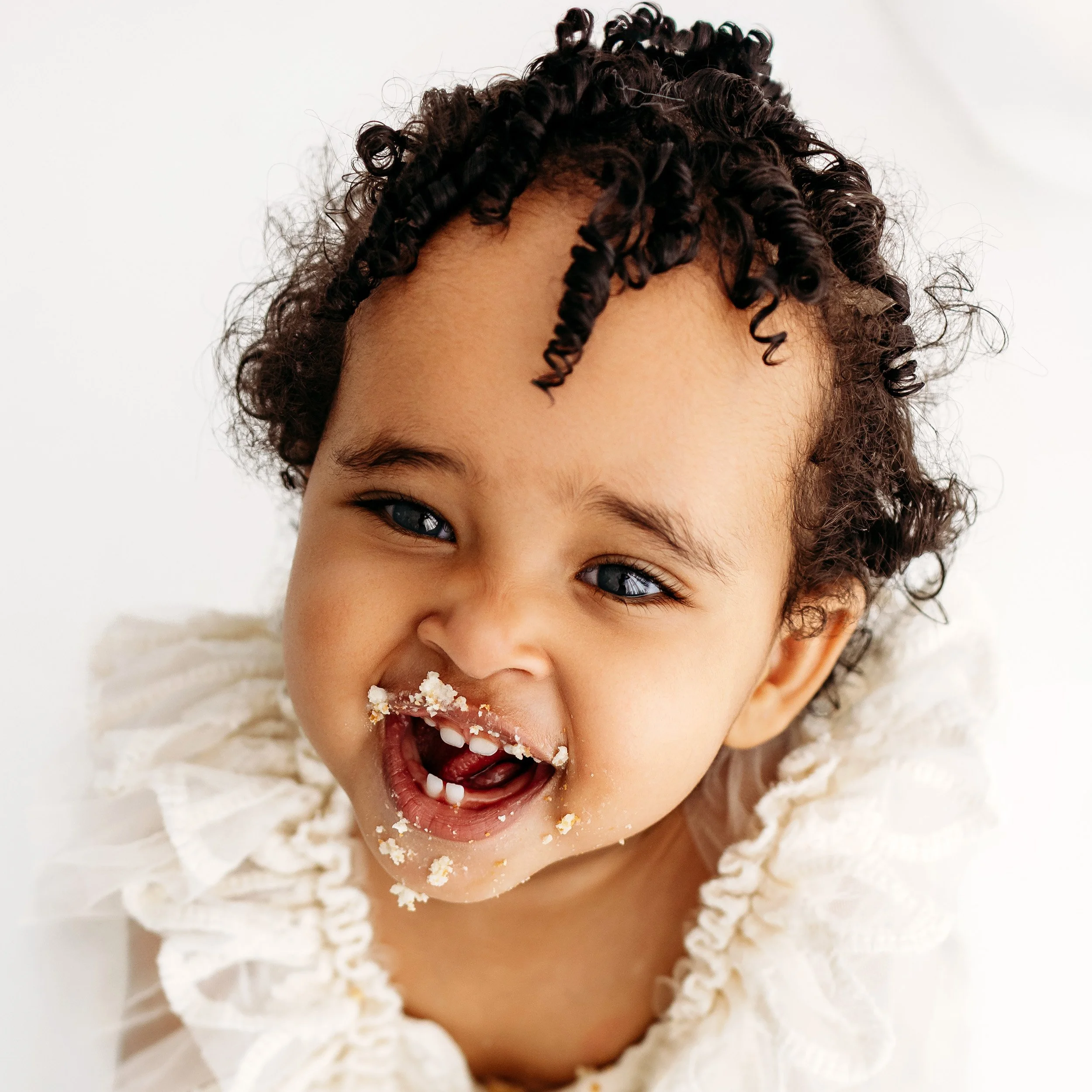 Smiling one-year-old with cake on her face during her first birthday cake smash.