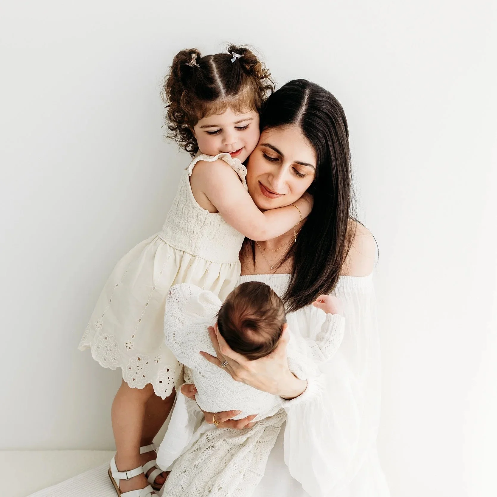 Mum cuddling her newborn baby and older child during a relaxed family newborn photography session in Perth.