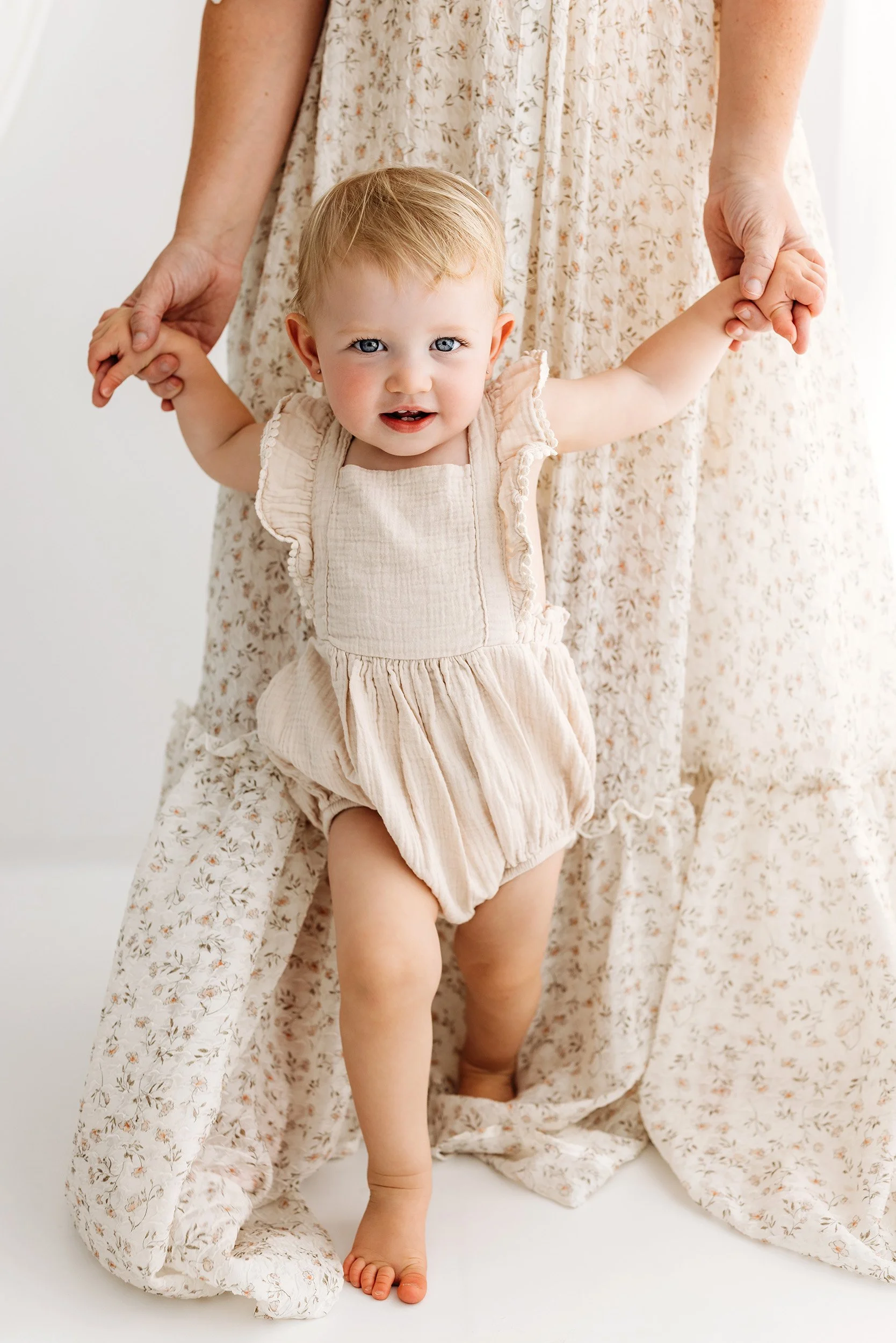 Baby standing while holding Mum's hands during a Motherhood Mini Session