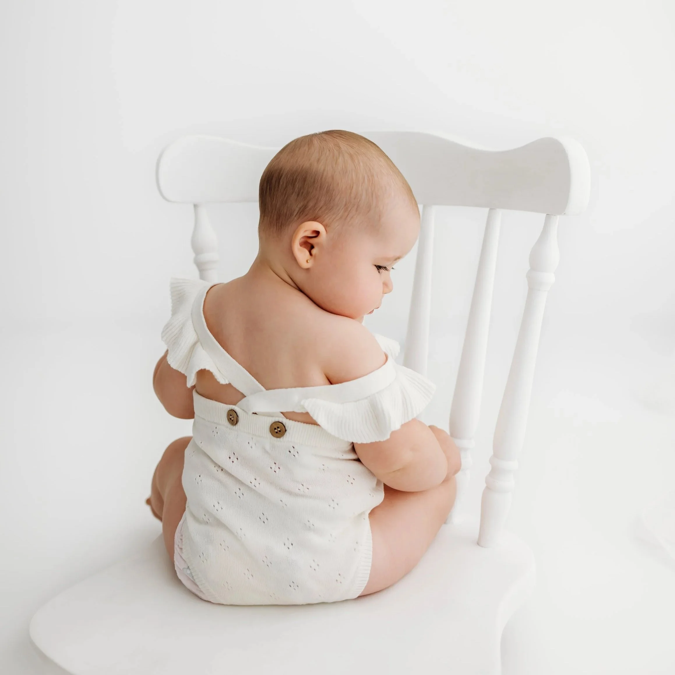Baby sitting independently on a white chair during a sitter photography session in Perth’s Swan Valley.