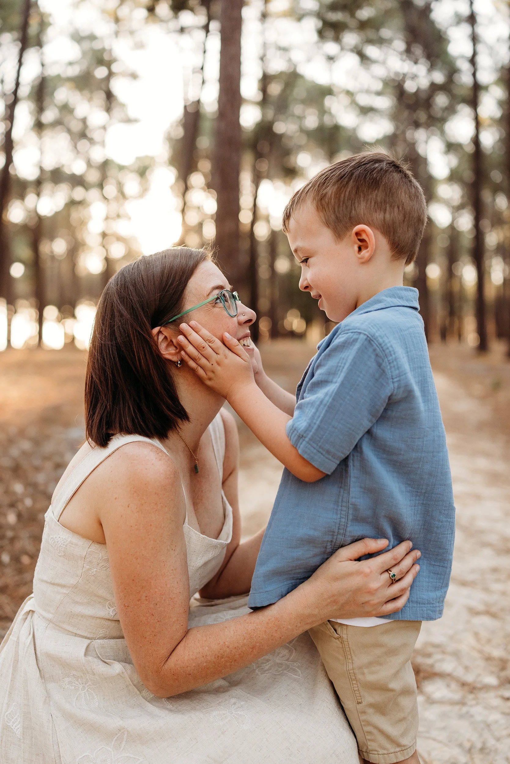 Mum smiling at her young son as he holds her face during an outdoor family photography session.