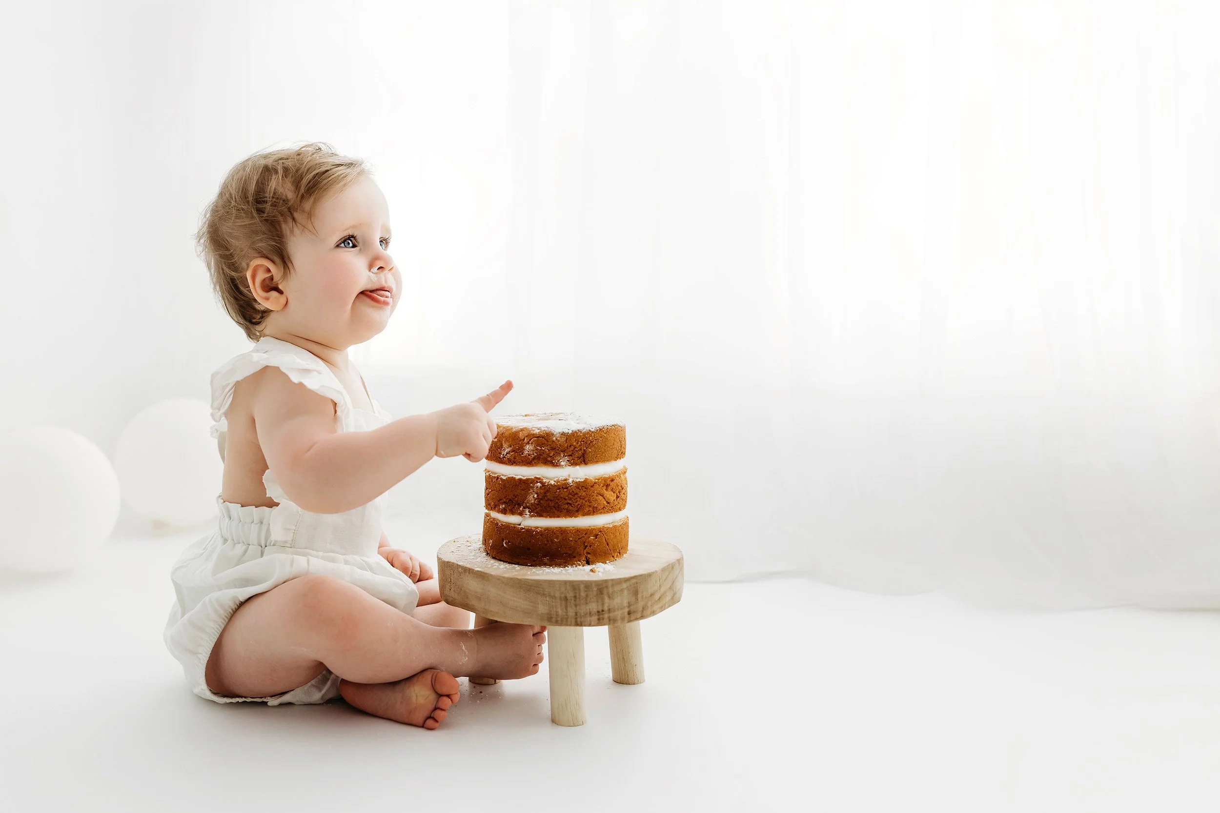 One-year-old baby sitting beside her first birthday cake in the Love Olive Photography studio.