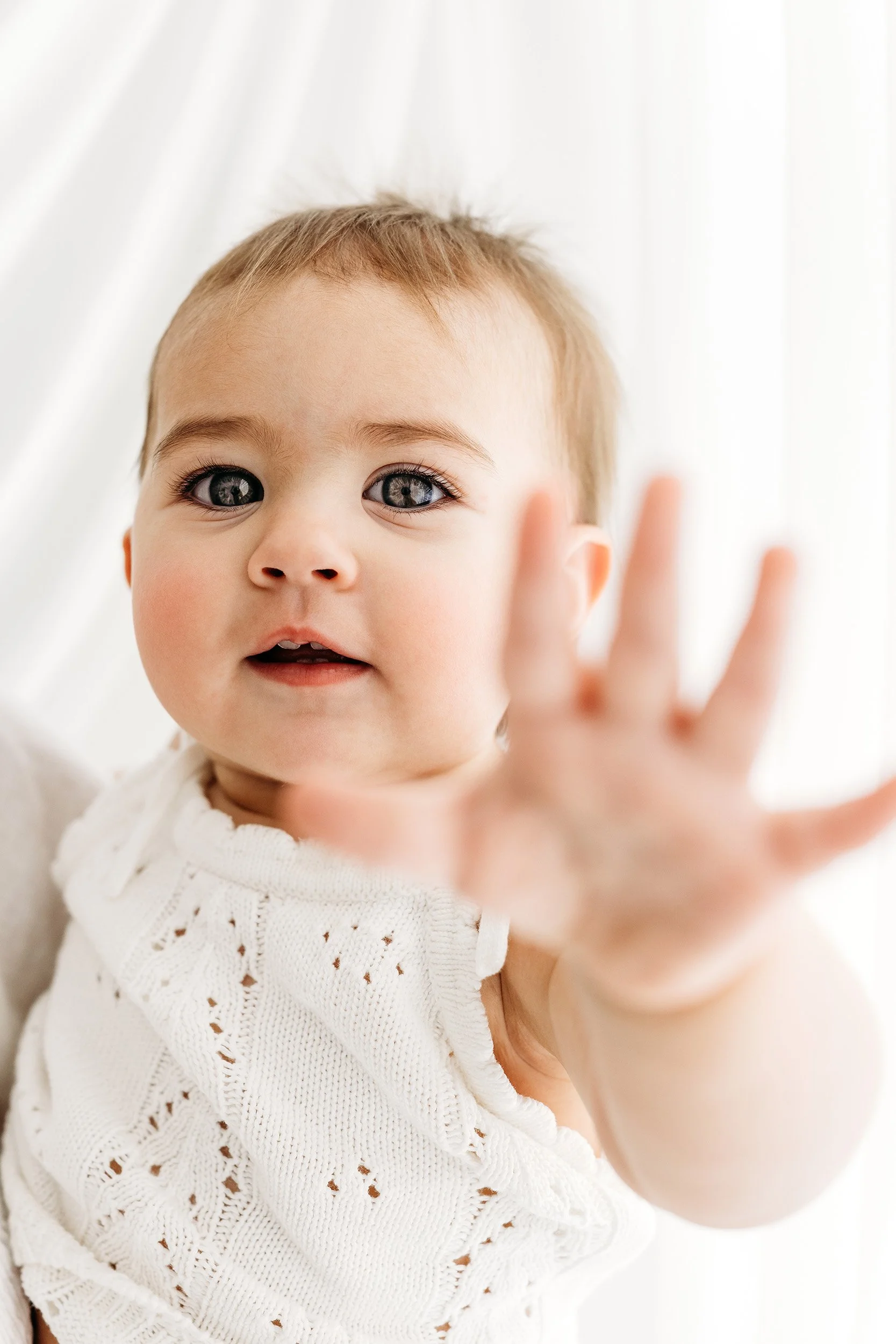 Baby reaching towards the camera during a relaxed milestone photography session in the Aveley studio.