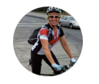 Another satisfied customer in cycling gear smiling with sunglasses, standing next to her bike, on a street or parking lot.