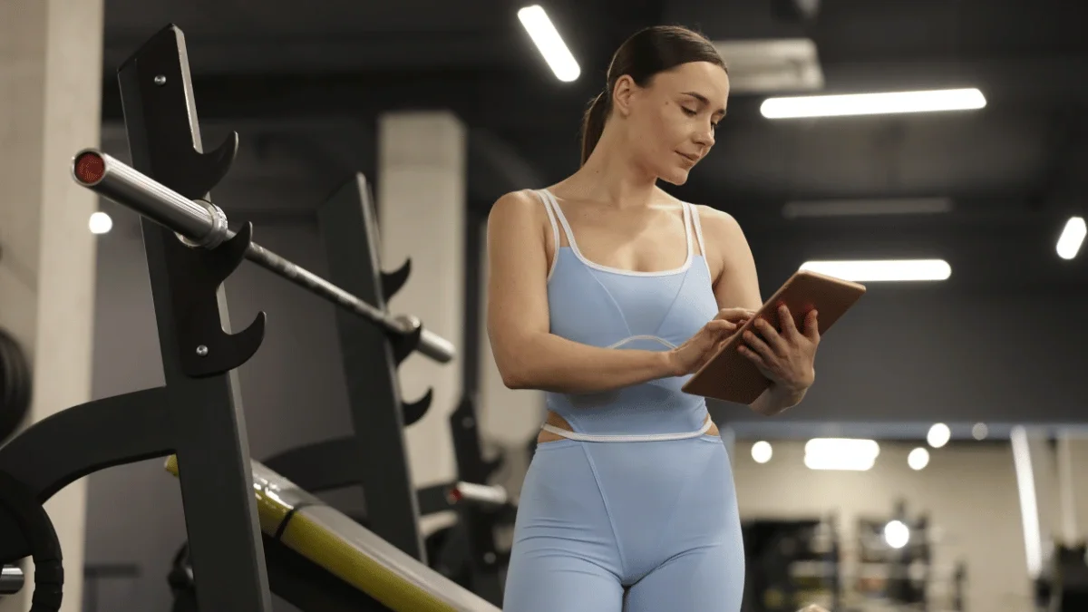 Woman reviewing a personalized workout program on a tablet while standing beside strength equipment in a modern gym.