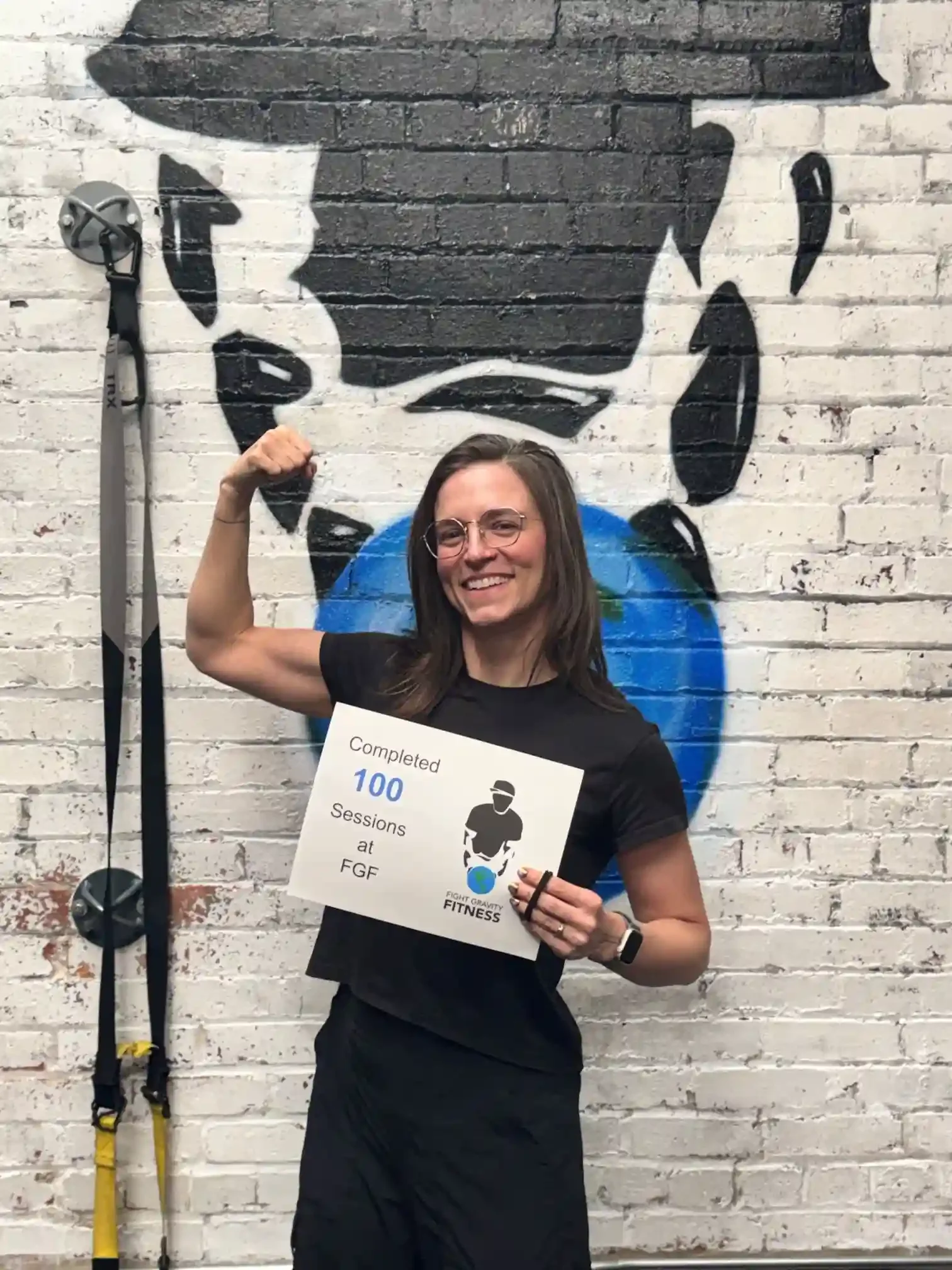 Fight Gravity Fitness member celebrating the completion of 100 personal training sessions while holding a milestone achievement certificate and flexing inside the gym.