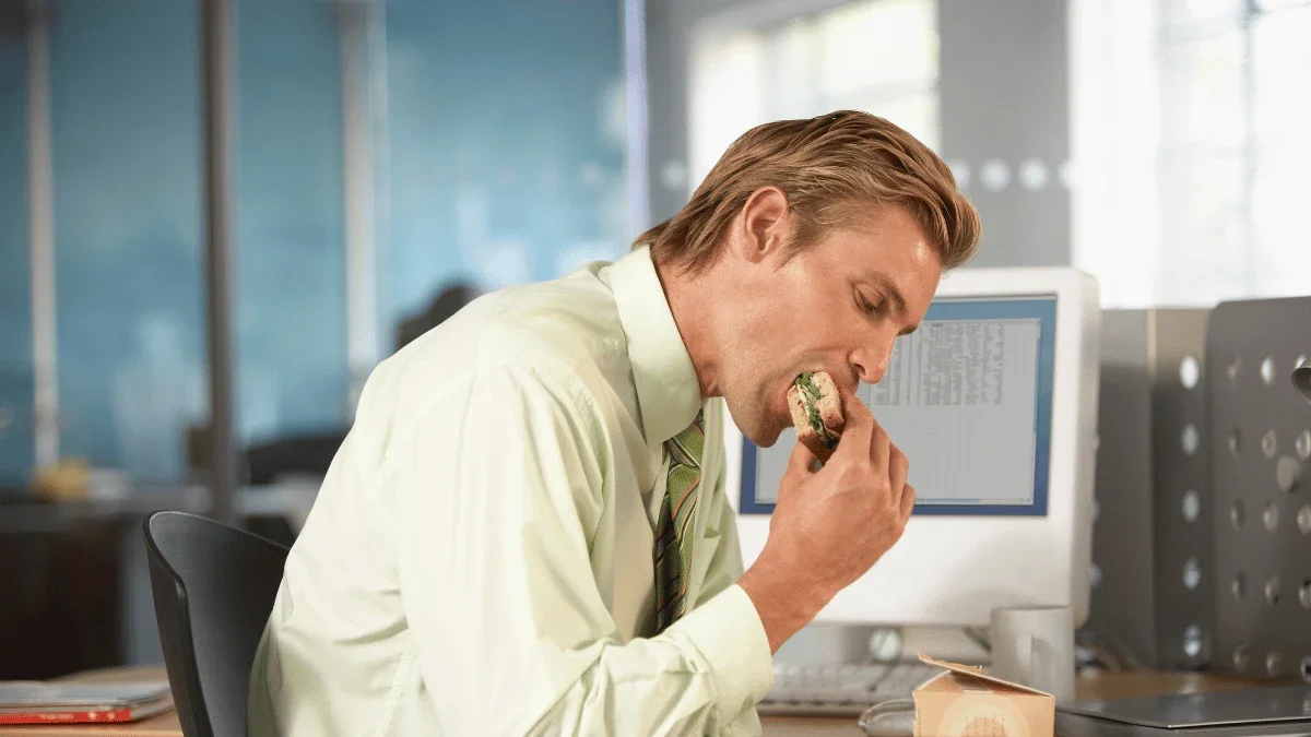 Busy office professional eating lunch at a desk while working at a computer during the workday.