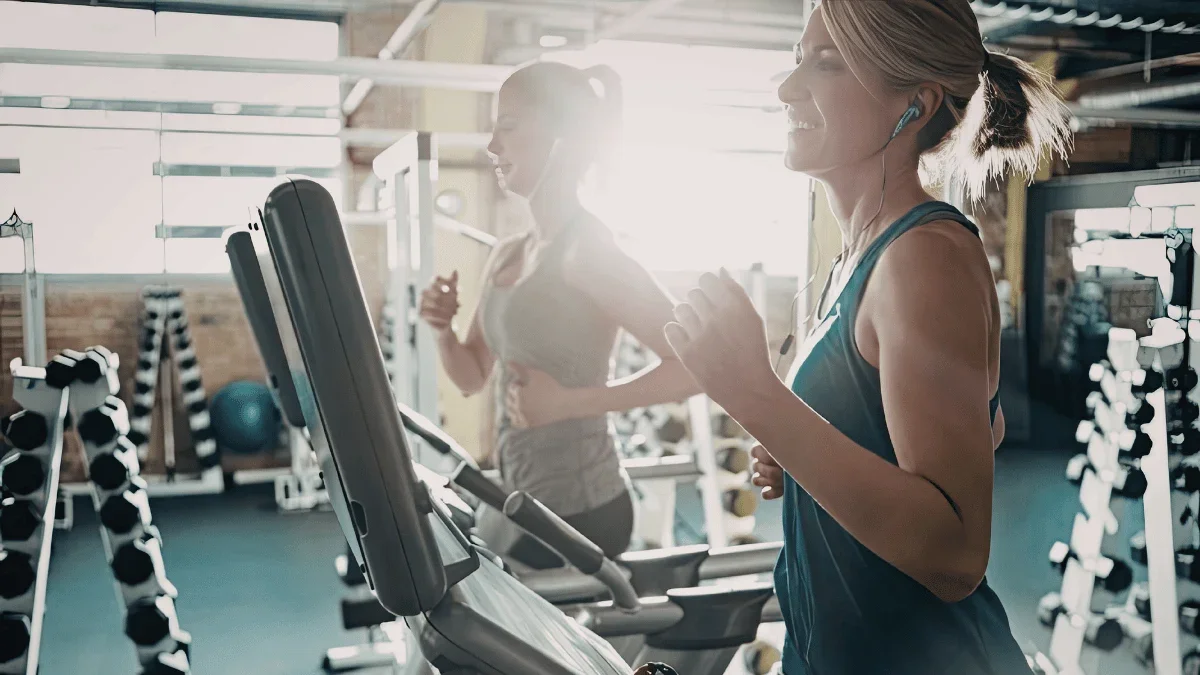 Two women jogging on treadmills inside a modern gym during a cardio workout session.