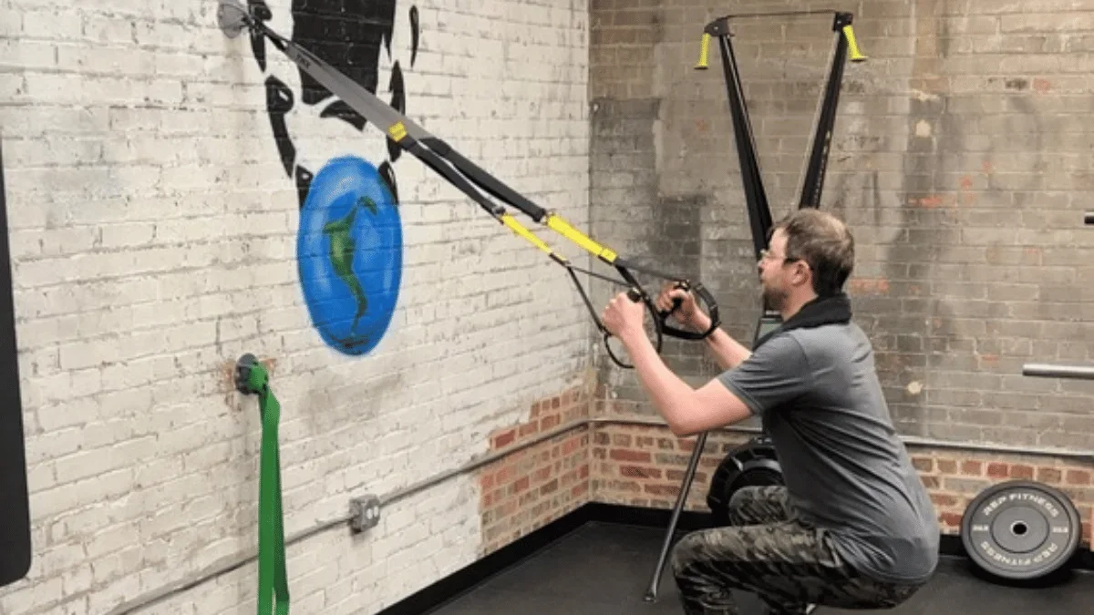 Man performing TRX squat exercise using suspension trainer in a private gym