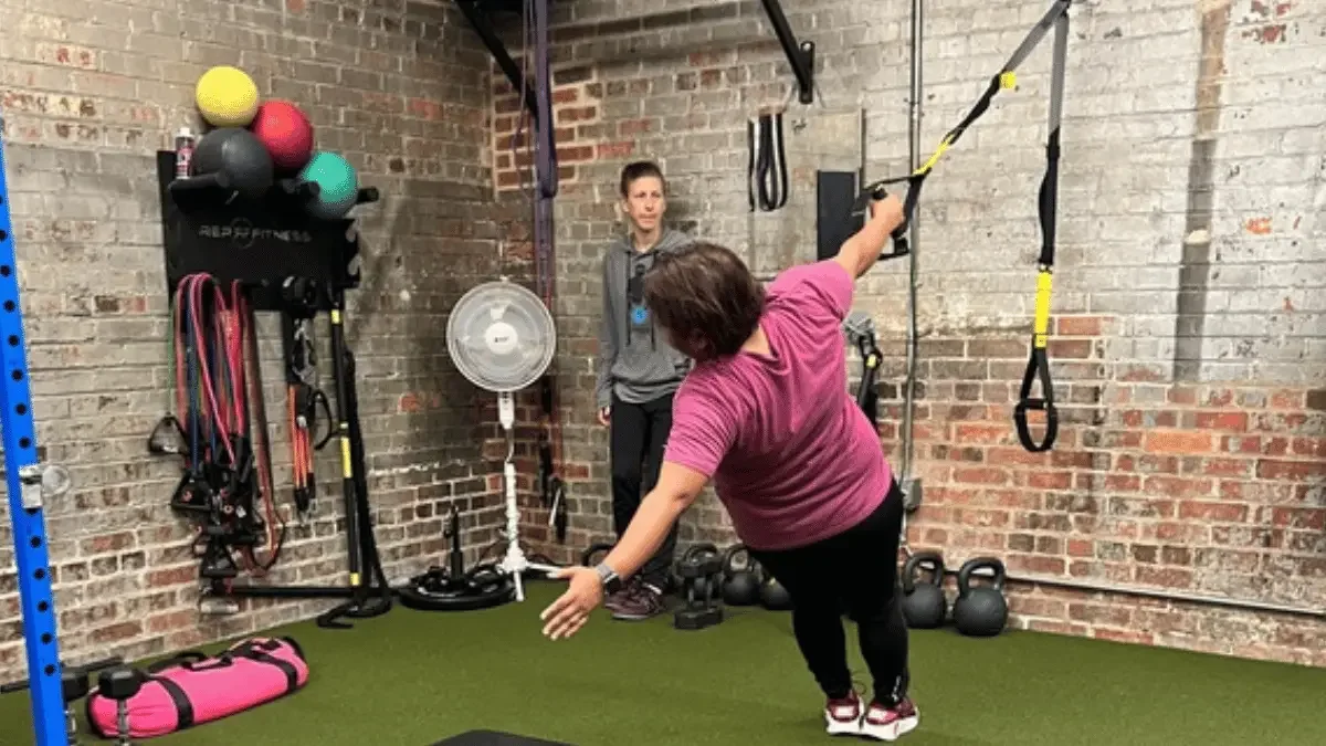 Woman performing a TRX balance exercise during a private personal training session in a gym.