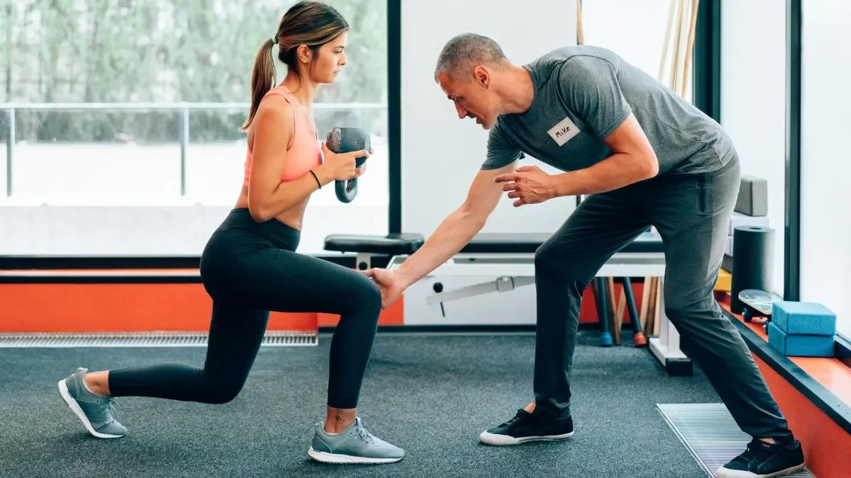 Trainer correcting form on a client doing weight lunge