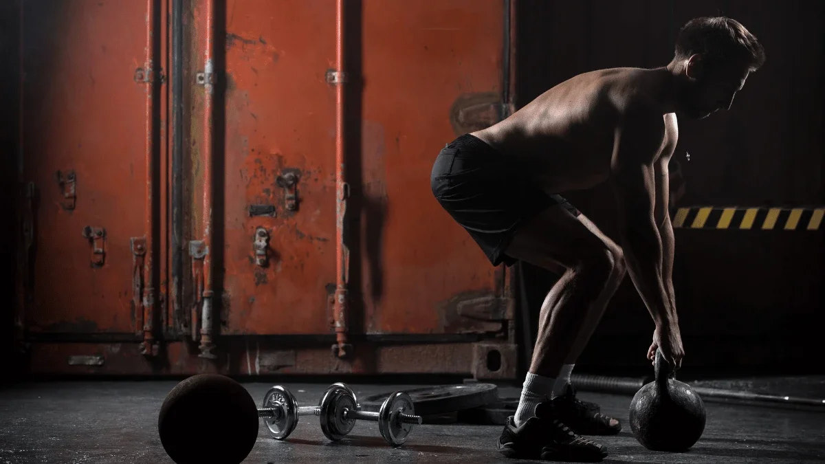 Athlete performing a kettlebell exercise during a full body strength training workout in an industrial-style gym.