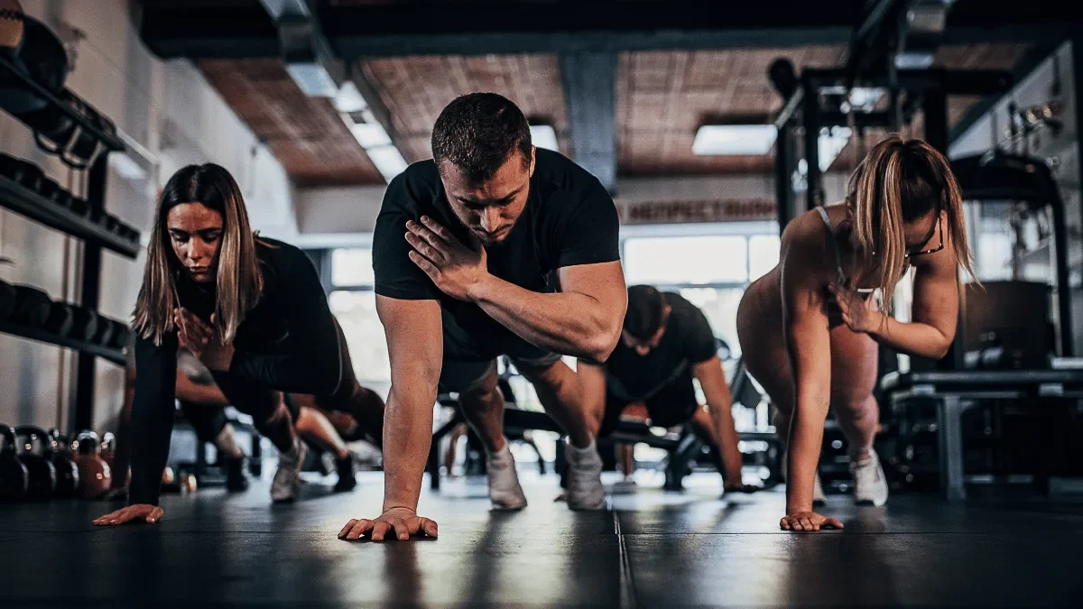 Group fitness participants performing plank exercises together during a structured training session in a gym.