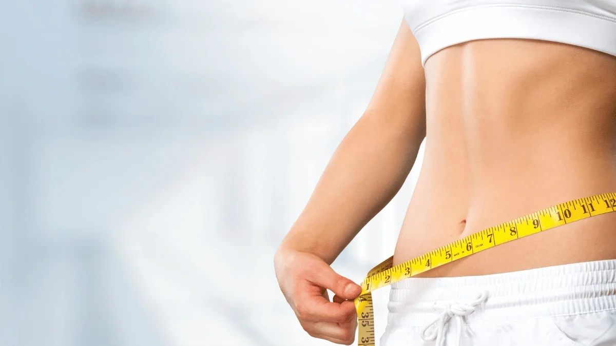 Close-up of a person measuring their waist with a tape measure to illustrate body recomposition and healthy weight management.