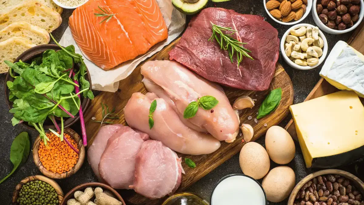 Assortment of high-protein foods including salmon, chicken, lean beef, eggs, cheese, lentils, nuts, and leafy greens for healthy nutrition.