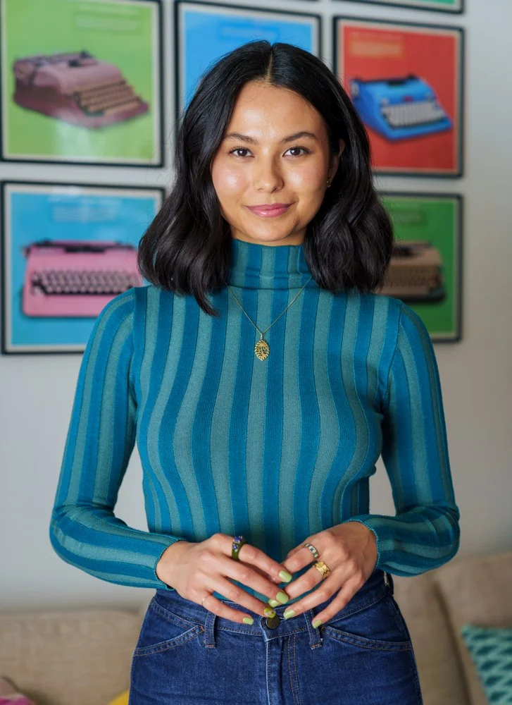Megan, a young Pasifika woman, standing up in front of typewriters with hands in front looking at camera